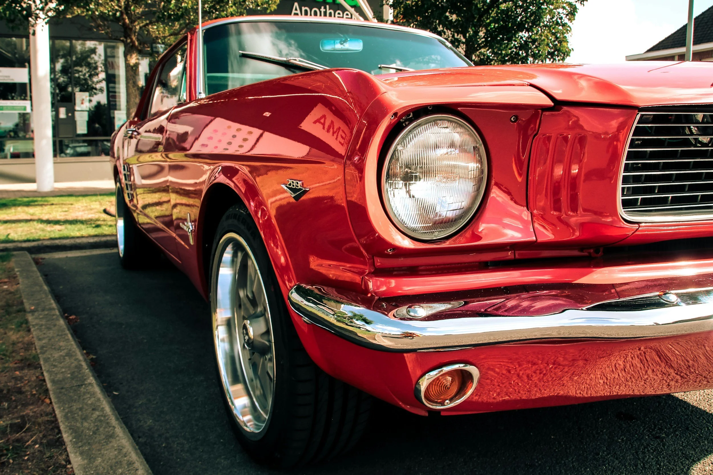 Close-up of a vintage red Chevrolet Corvette parked on a street, with reflections on its shiny surface and a building with signs in the background.