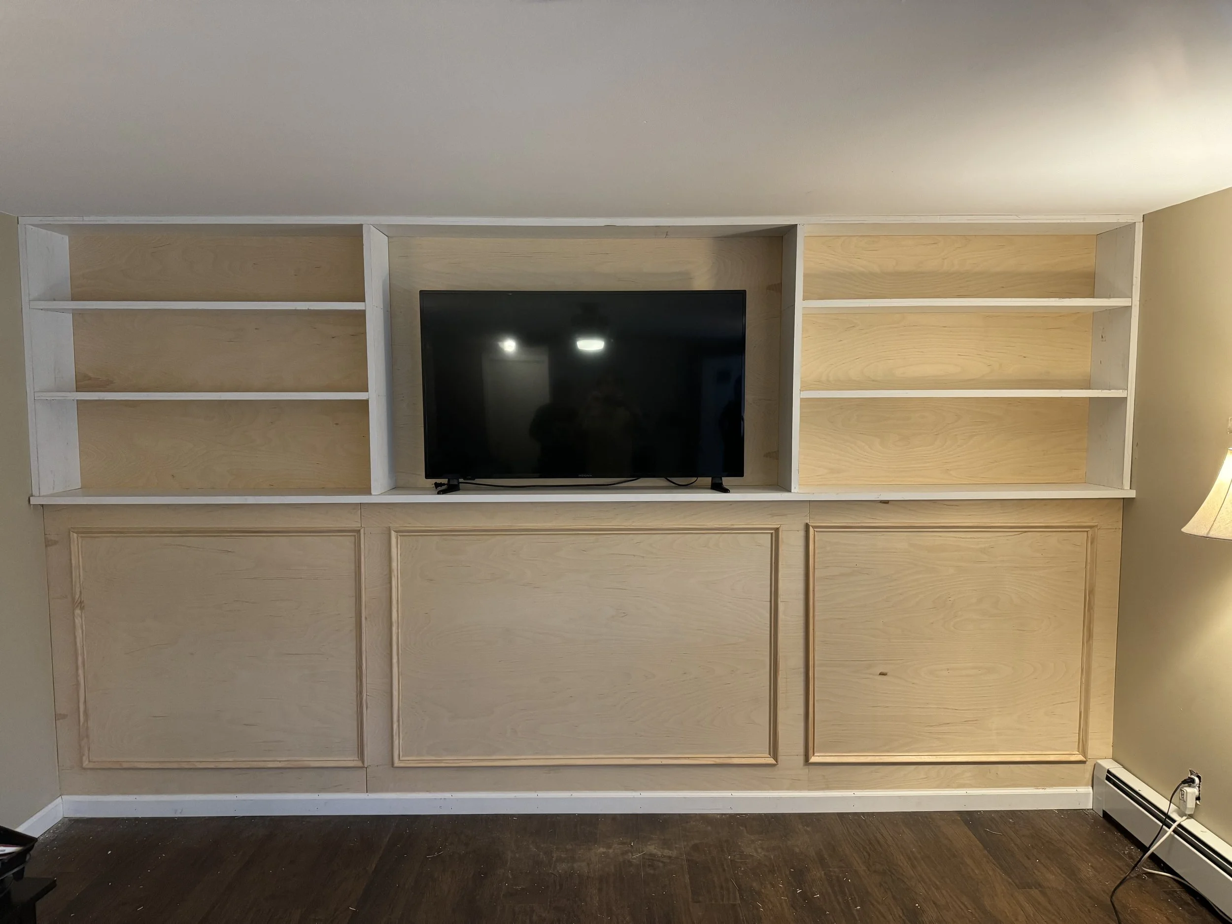 Empty wooden built-in shelves in a room with a black television in the center and a lamp on the right side.