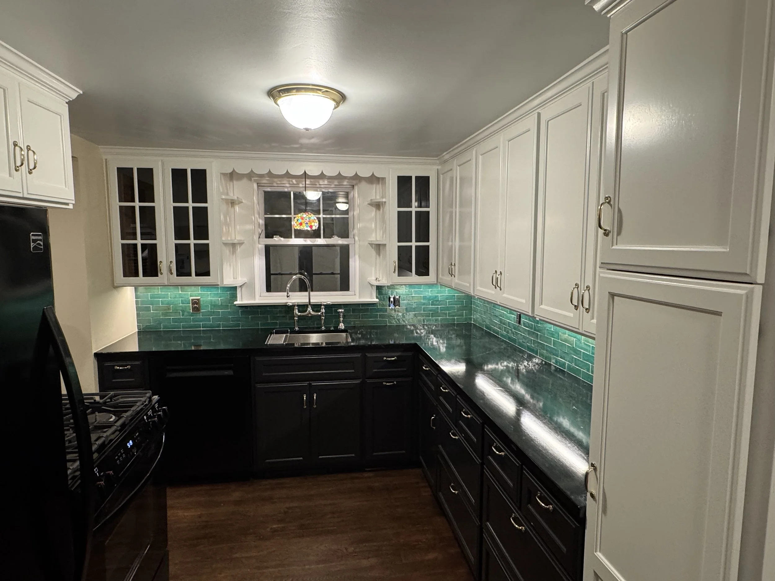 A kitchen with white cabinets, a green tile backsplash, a window, and a black countertop with a sink.