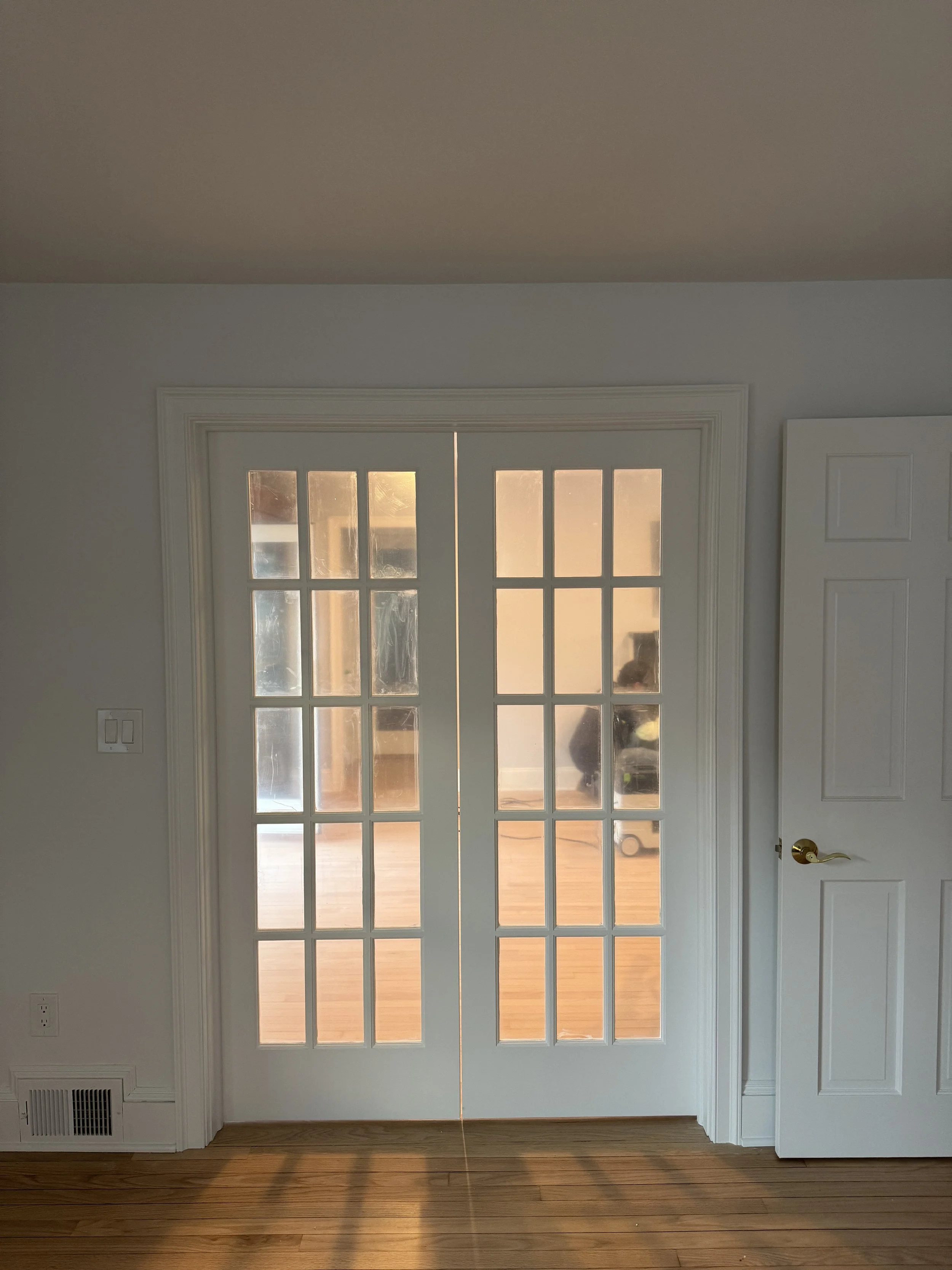 Living room with white French doors and hardwood floor, sunlight coming through the glass panels, white walls, and a white ceiling.