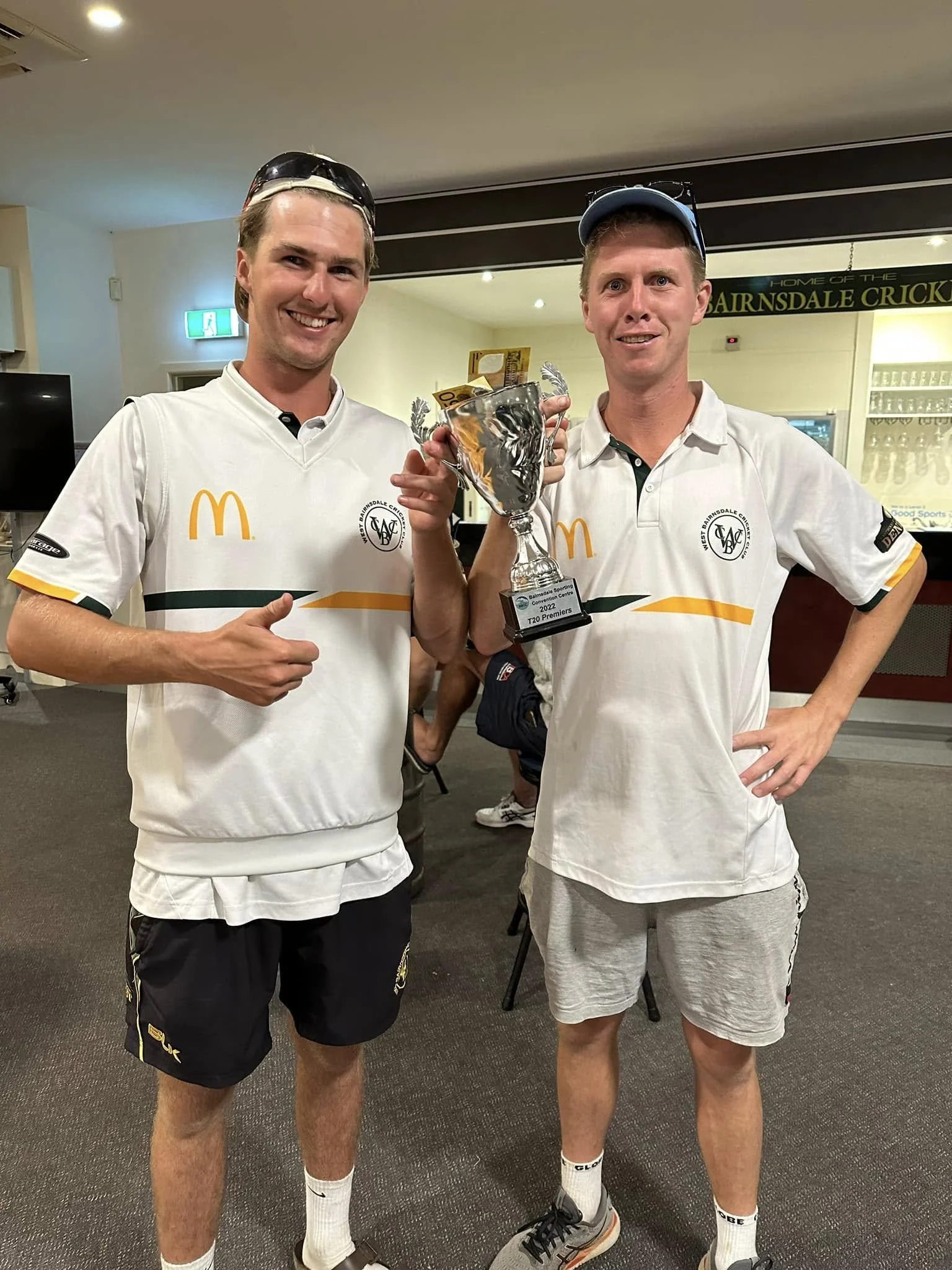 Two young men in sports uniforms holding a trophy and celebrating indoors.