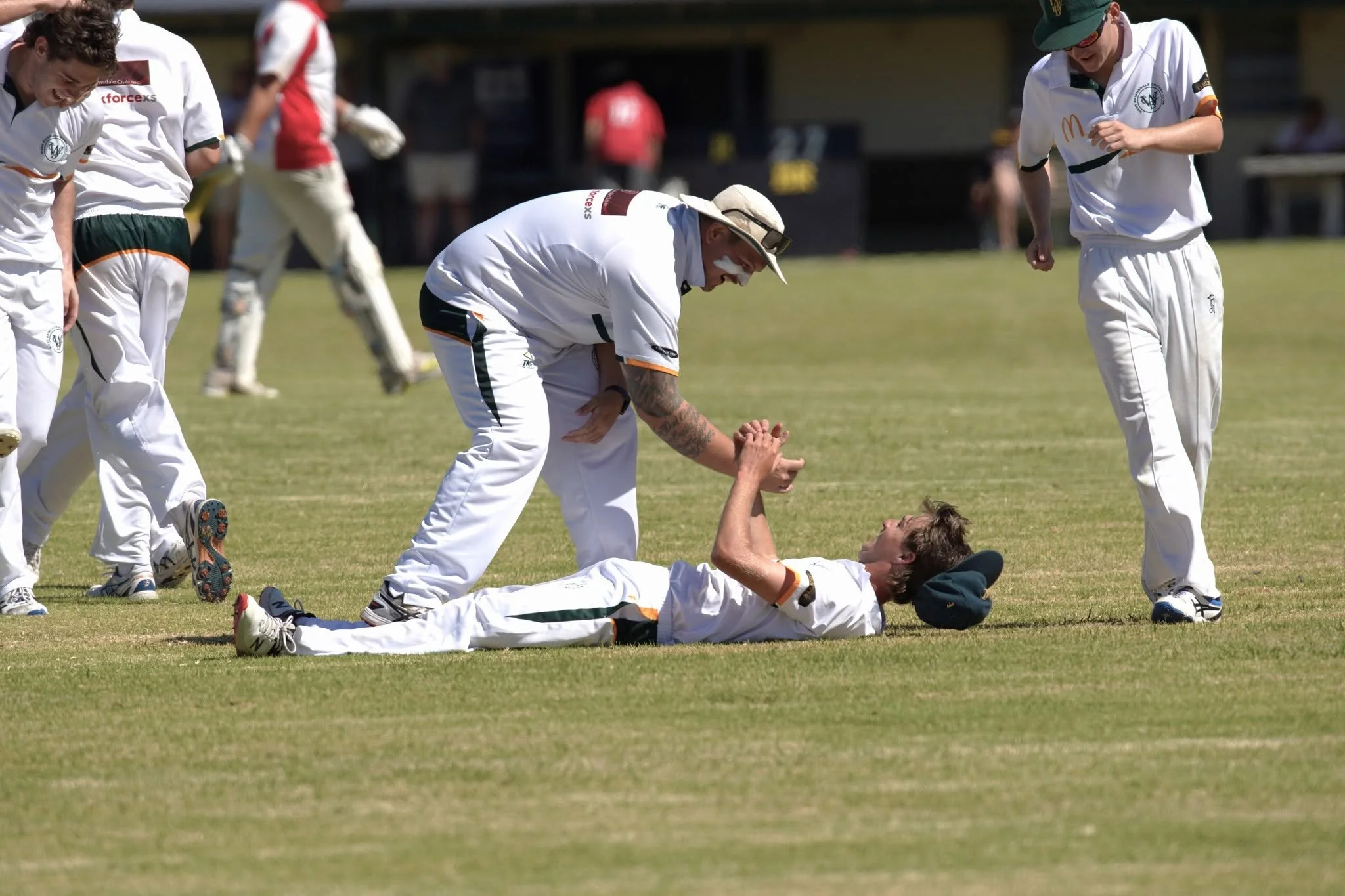 Cricketers on the field assisting an injured teammate lying on the ground during a match.