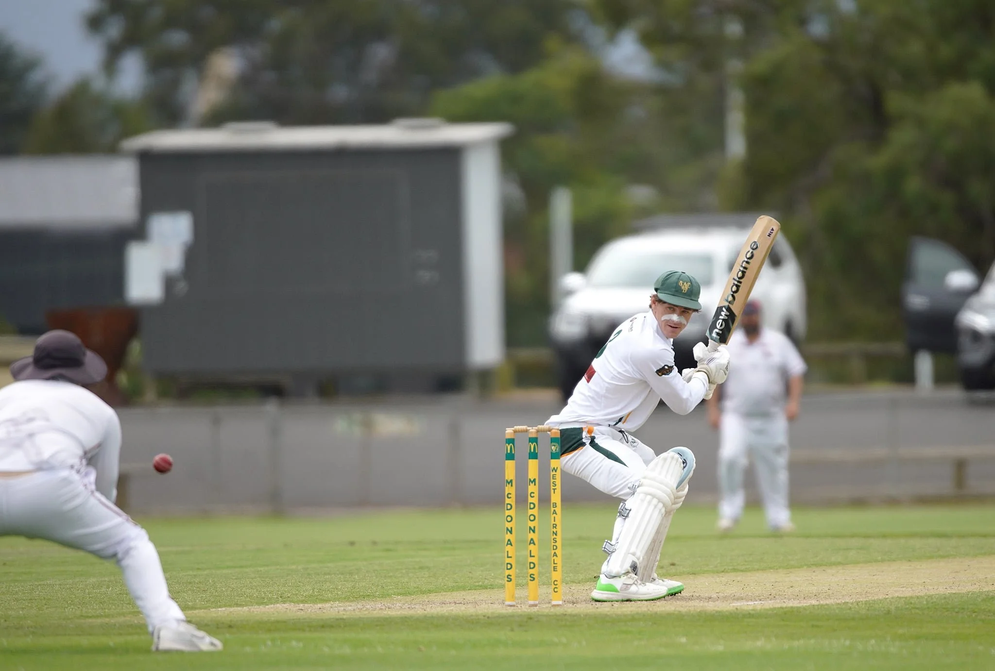 A cricket player in white uniform and a green cap batting on a cricket field during a match.