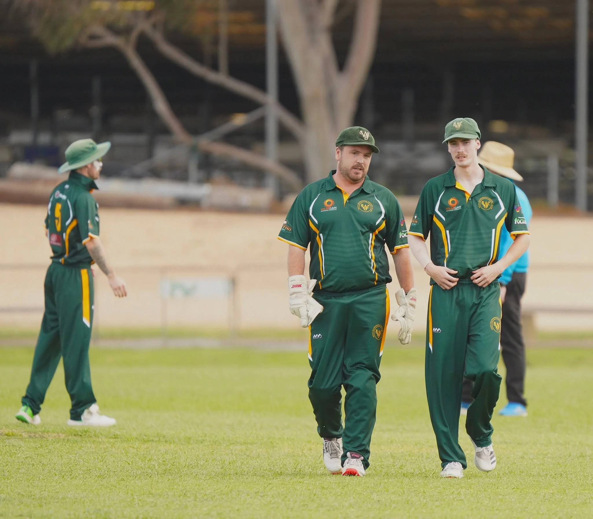 Cricket players in green uniforms walking on a cricket field.