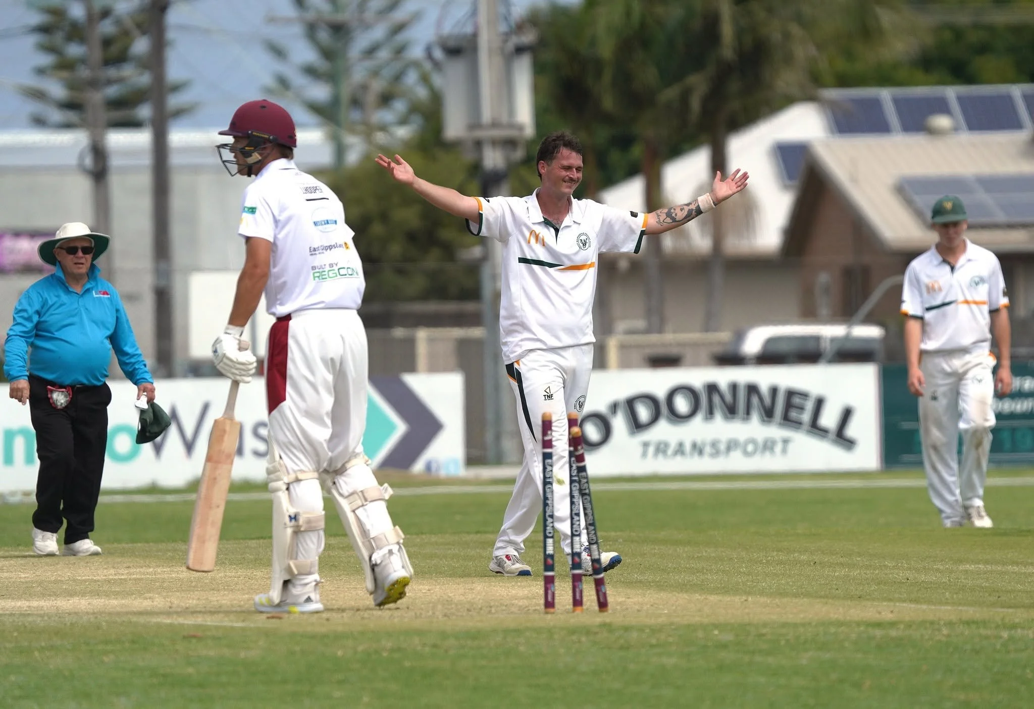 Cricket players on the field during a match, with one player smiling and raising his arms, and others walking nearby.