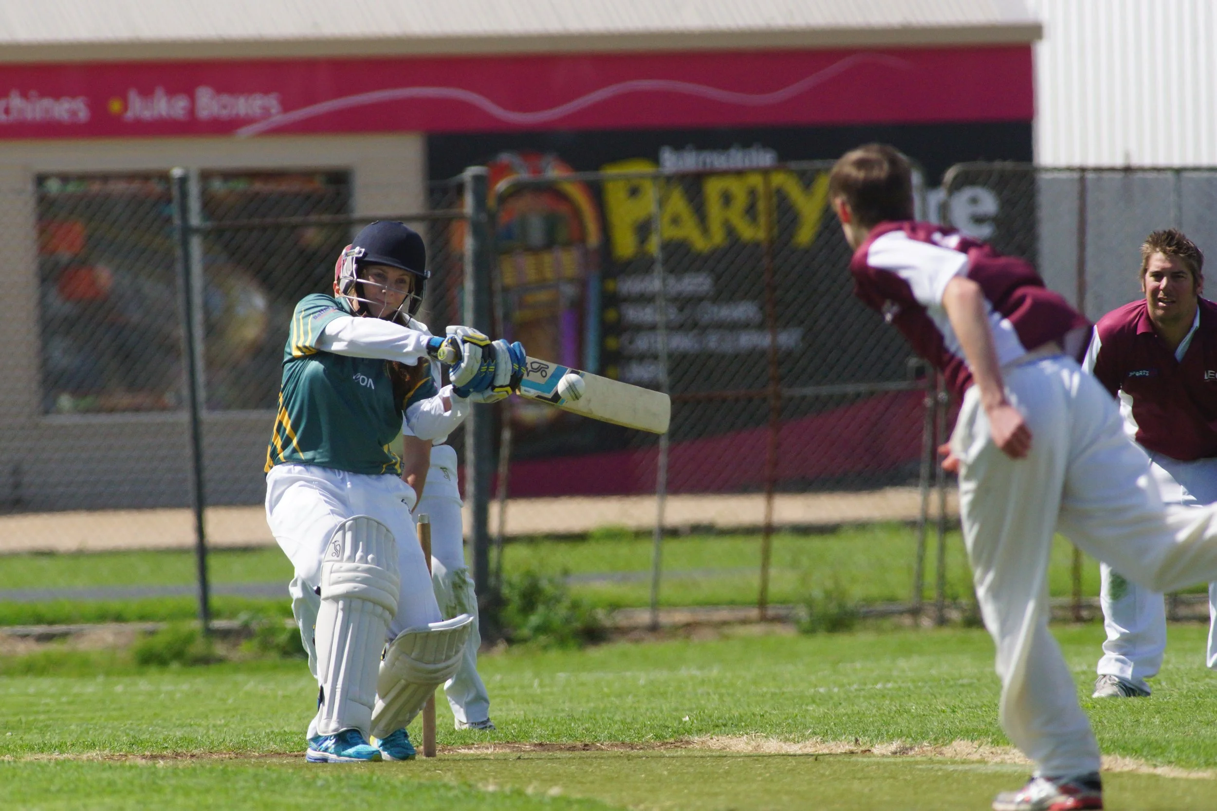A cricket game with players on the field, one player preparing to hit the ball while others are in position.