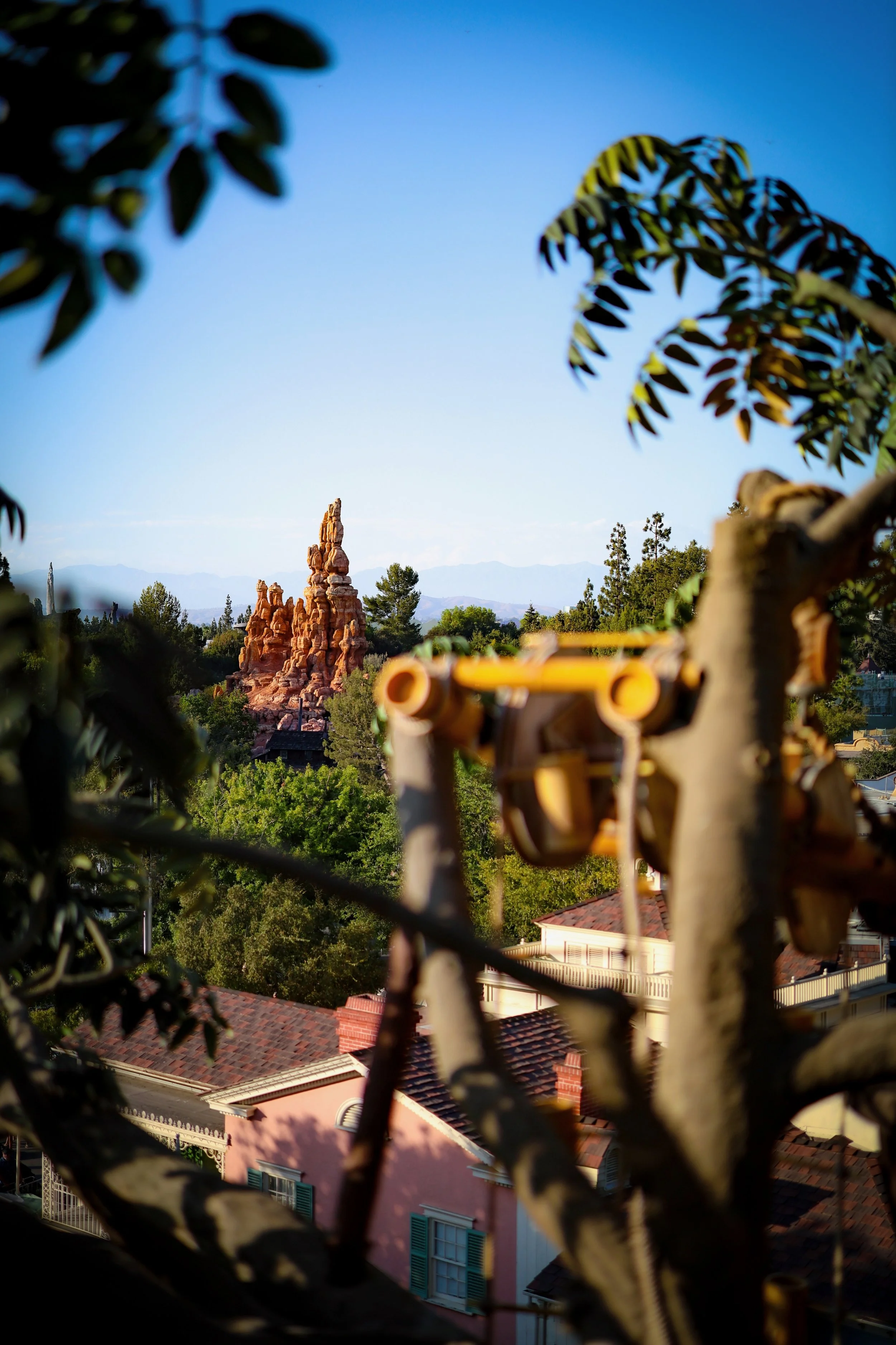 View of a desert rock formation seen through a metal balcony railing with plants in the foreground and residential rooftops below.