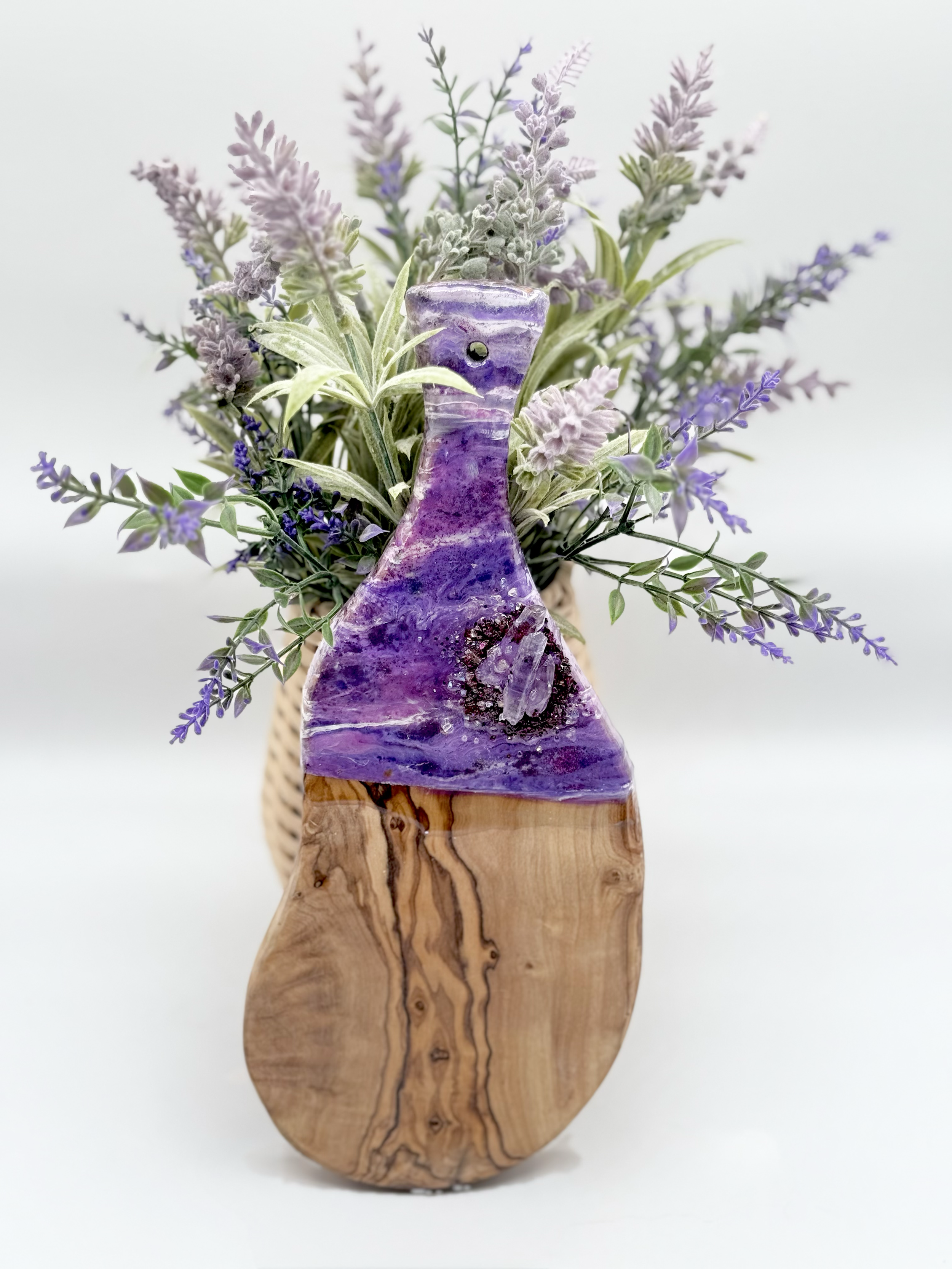 A wooden vase with embedded purple and white stones, holding a bouquet of lavender and other purple flowers.
