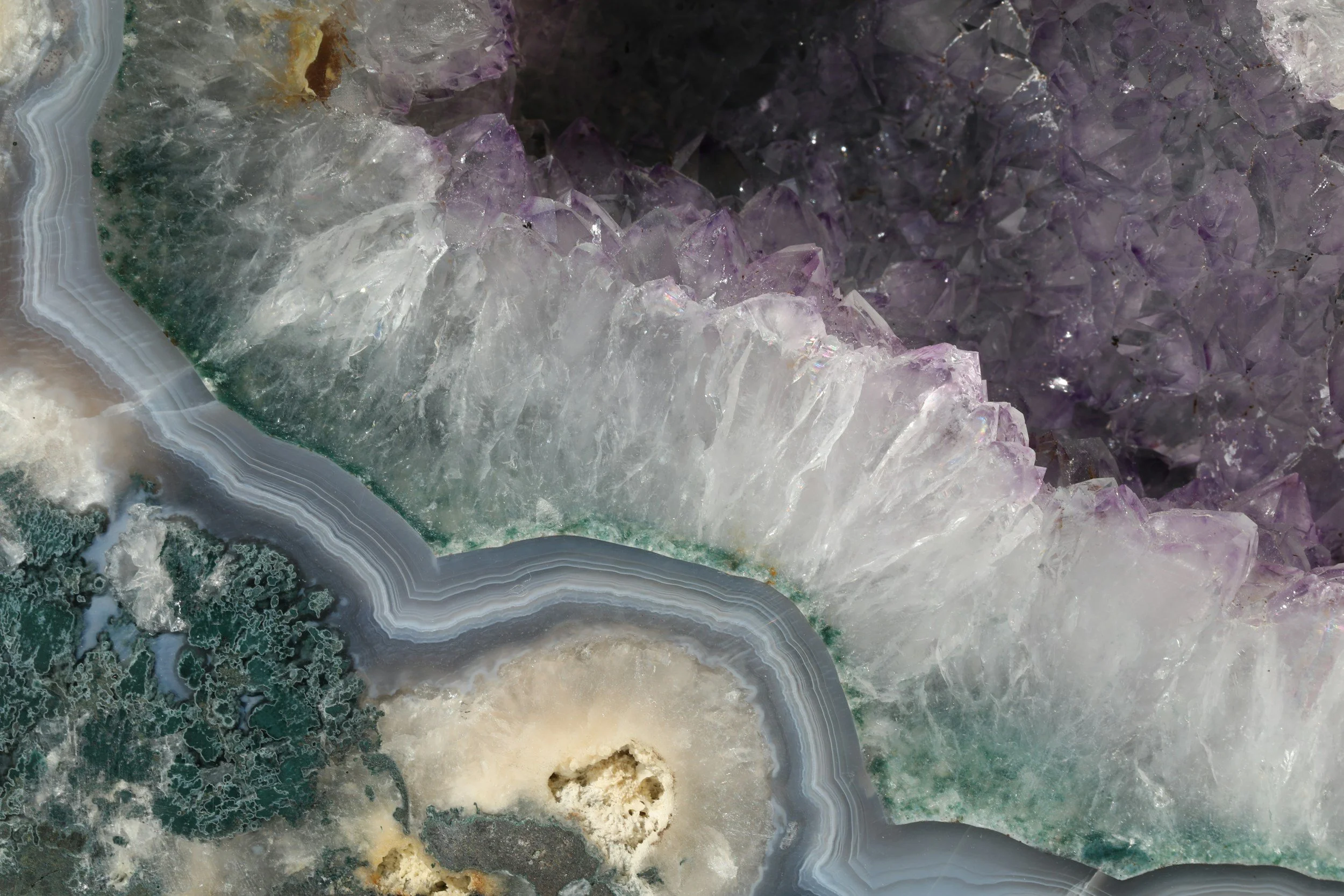 Close-up of a colorful geode with purple, white, and black crystalline formations, and banded layers of mineral deposits.