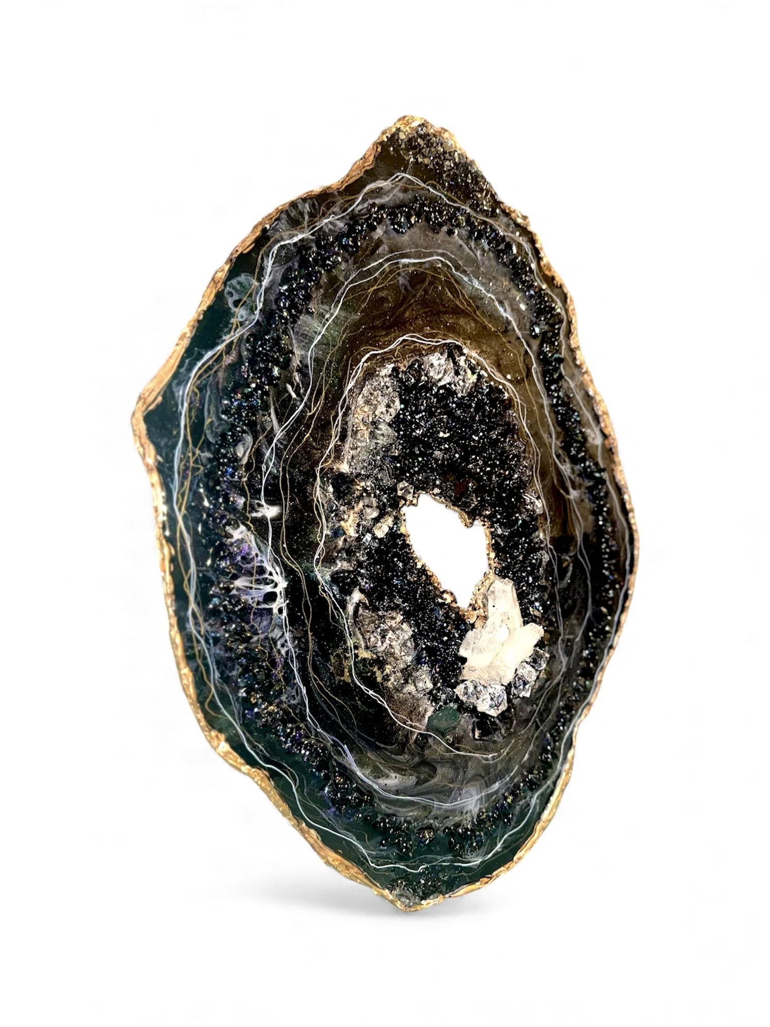 An ornate polished geode with a gold edge, showing dark crystal interior with sparkling crystals, laid against a white background.