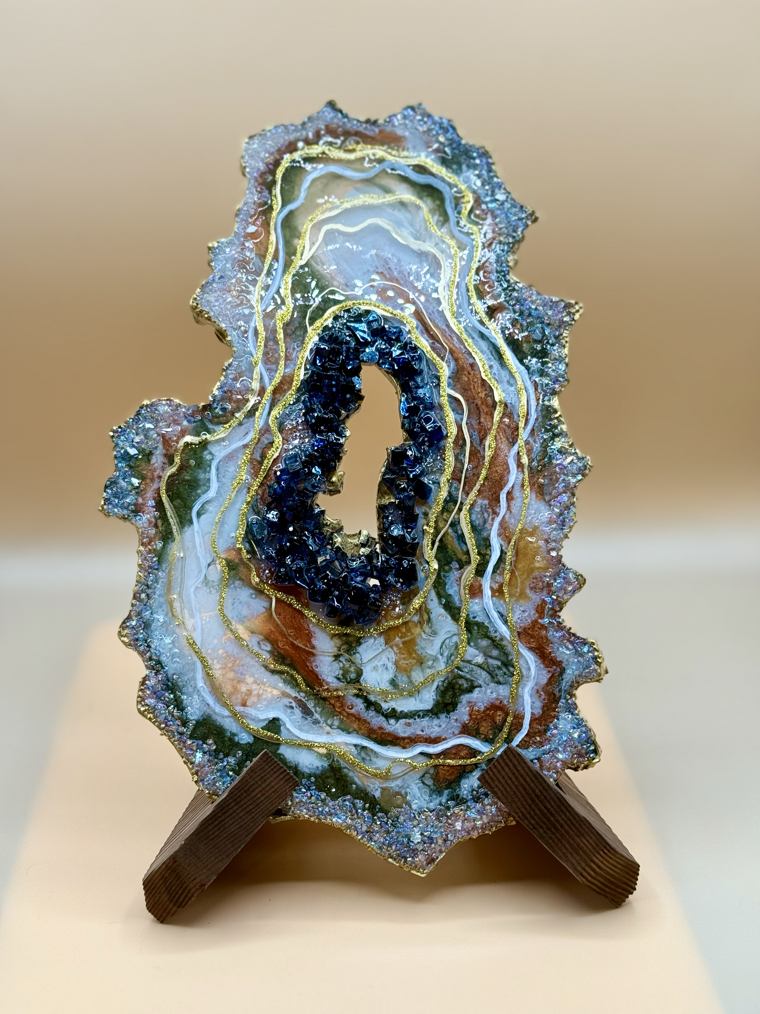 A colorful, abstract piece of art resembling an agate slice with intricate patterns, glitter, and gold accents, mounted on a brown strap.