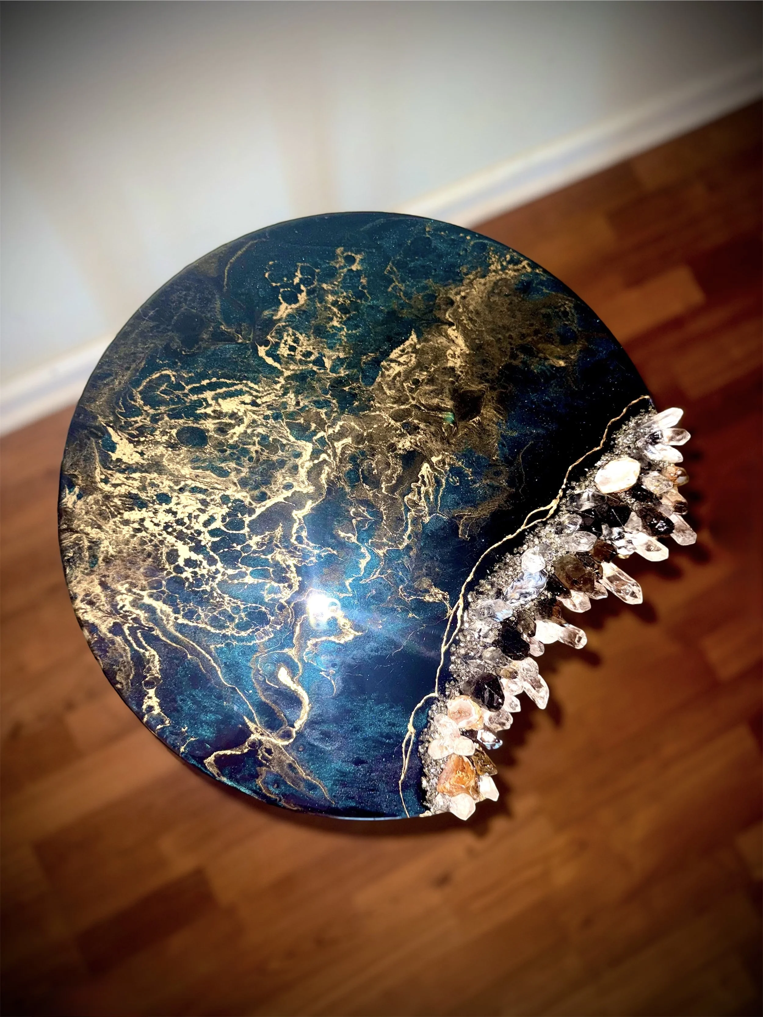 Close-up of a blue and gold marble-like decorative object with crystals on the edge, resting on a wooden surface.