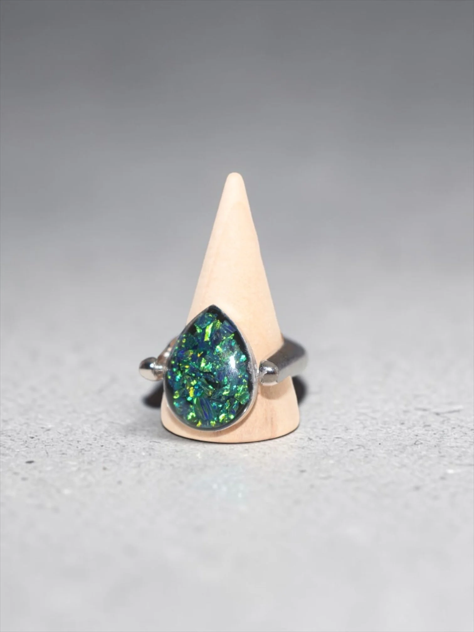 Close-up of a ring with a colorful, iridescent stone, displayed on a ceramic ring holder with a beige cone shape.