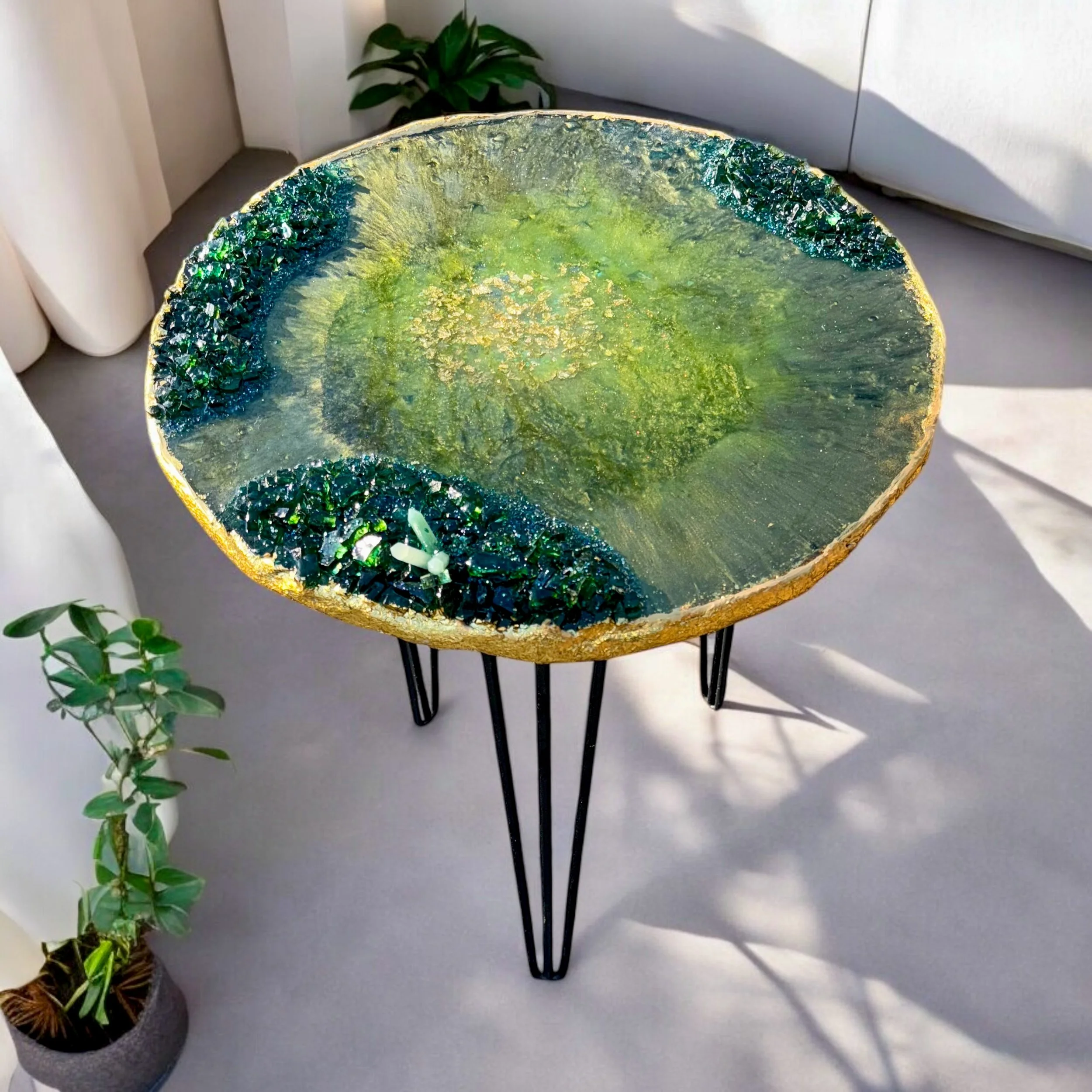 Decorative table with a green, textured surface and black metal legs, positioned on a gray floor with indoor plants nearby.