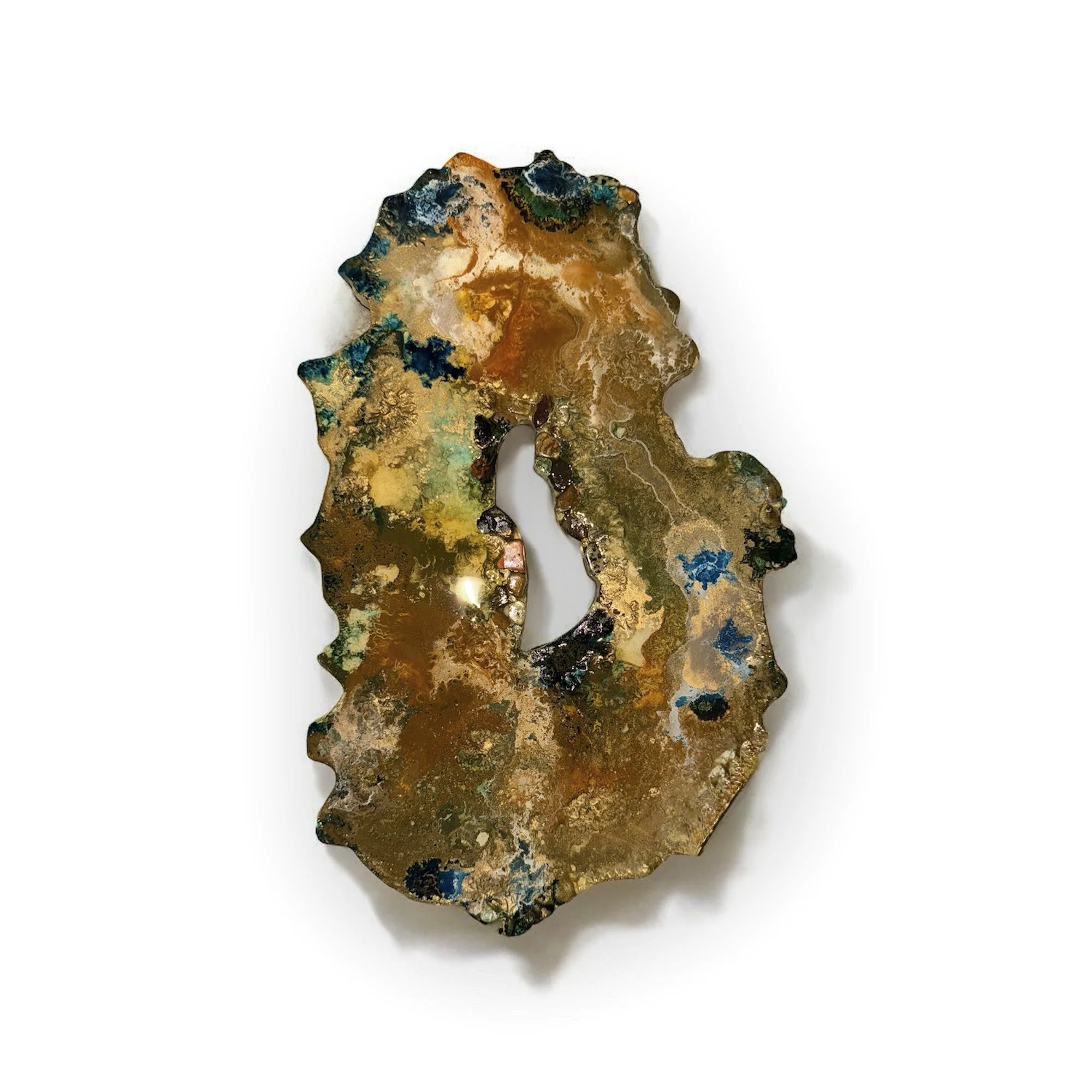 An abstract, irregular-shaped piece of art with multicolored metallic and iridescent surfaces, predominantly featuring shades of gold, blue, green, and black, set against a plain white background.