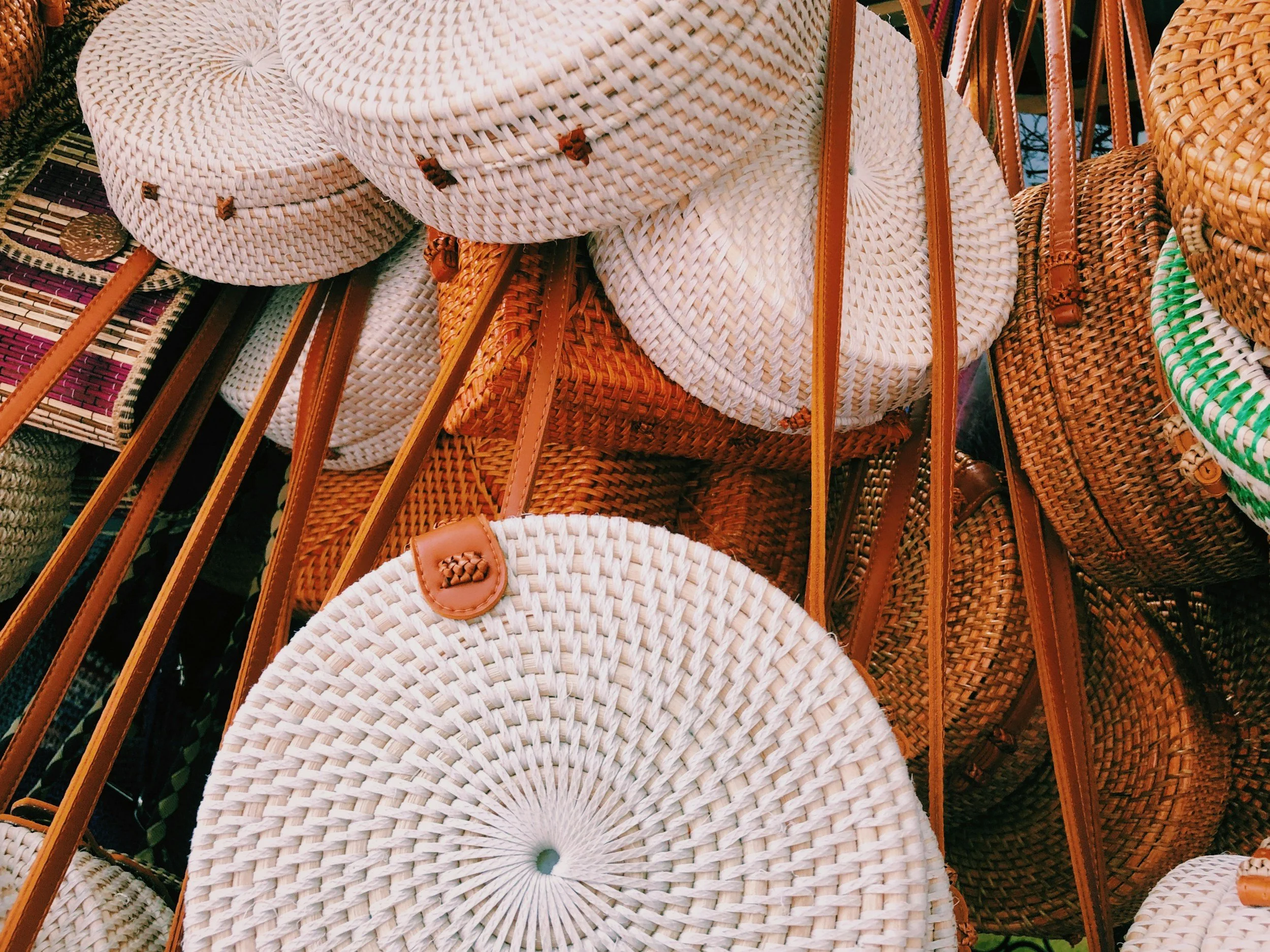 A display of woven straw handbags and shoulder bags with leather straps arranged on a surface, showcasing natural materials and craftsmanship.