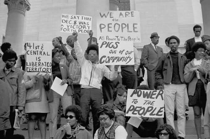 Black and white photo of a protest with people holding signs advocating for community empowerment, civil rights, and the release of political prisoners.