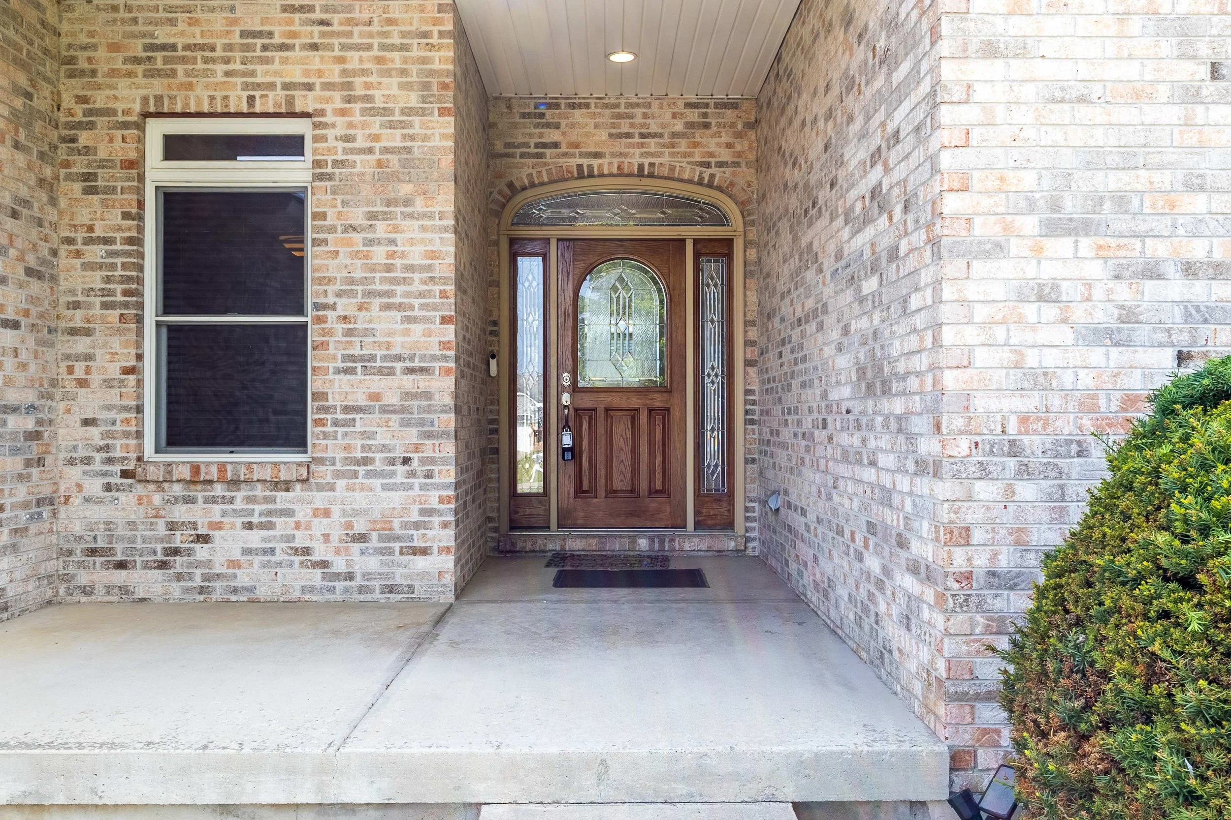 Front entrance of a house with a brick facade, a wooden door with decorative glass panels, and a small window to the left of the door.
