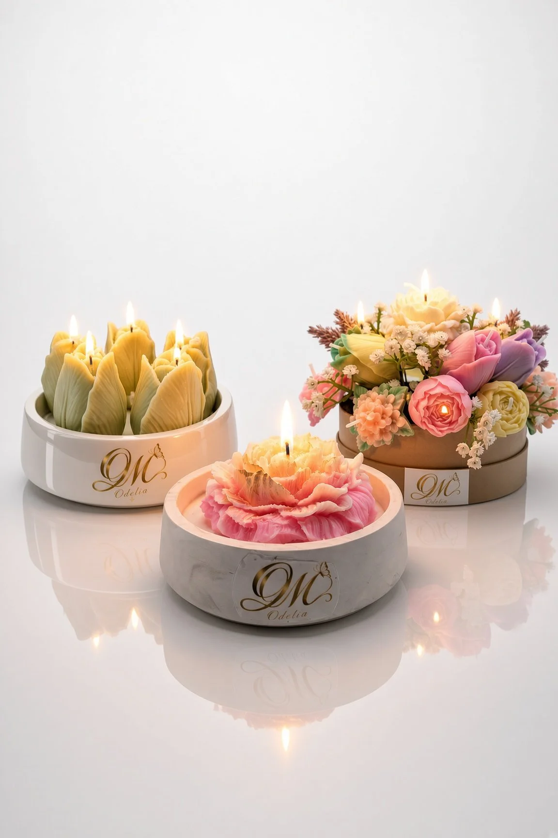Three lit ODazzled candle arrangements: yellow tulip candles in a white bowl, pink peony candle in a marble bowl, and pastel flower bouquet with candles in a tan Odelia box