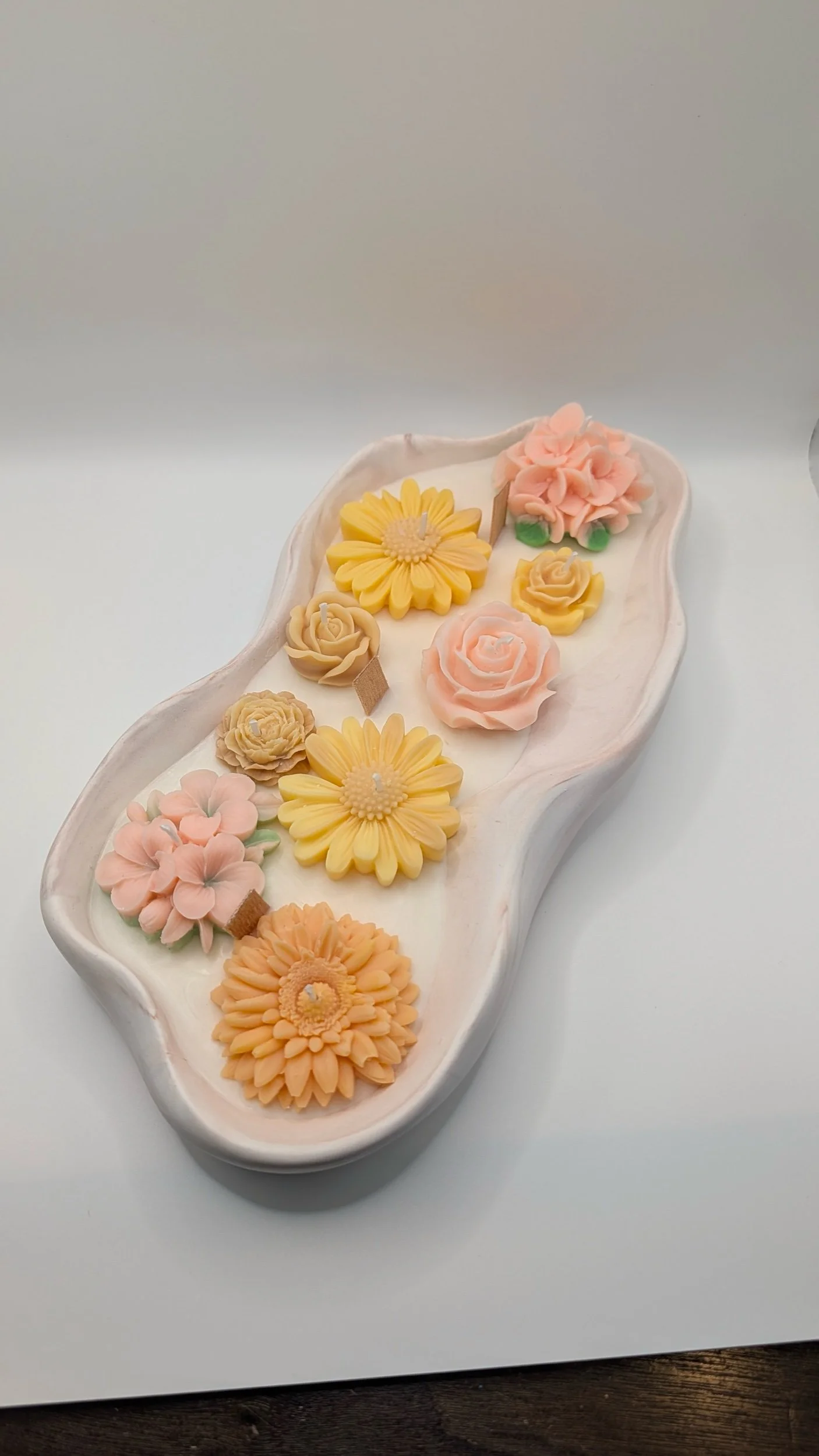 White ceramic tray with colorful flower-shaped candles: yellow daisies, pink roses, orange dahlias and peach blooms