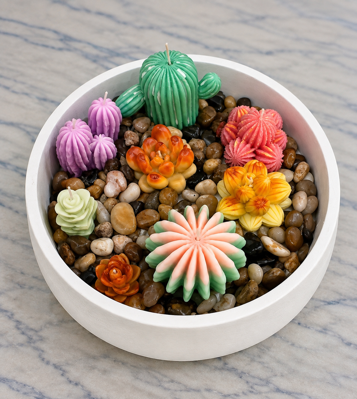 Colorful cactus and succulent-shaped candles in green, purple, orange, pink and yellow arranged in a white bowl with pebbles