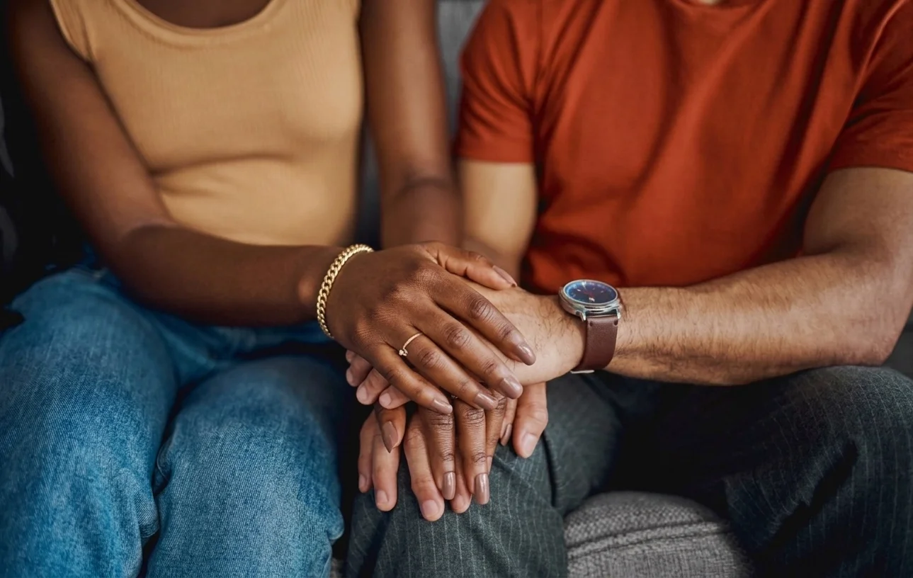 Close-up of a couple holding hands, with one person's hand resting on top of the other's, depicting support and connection.