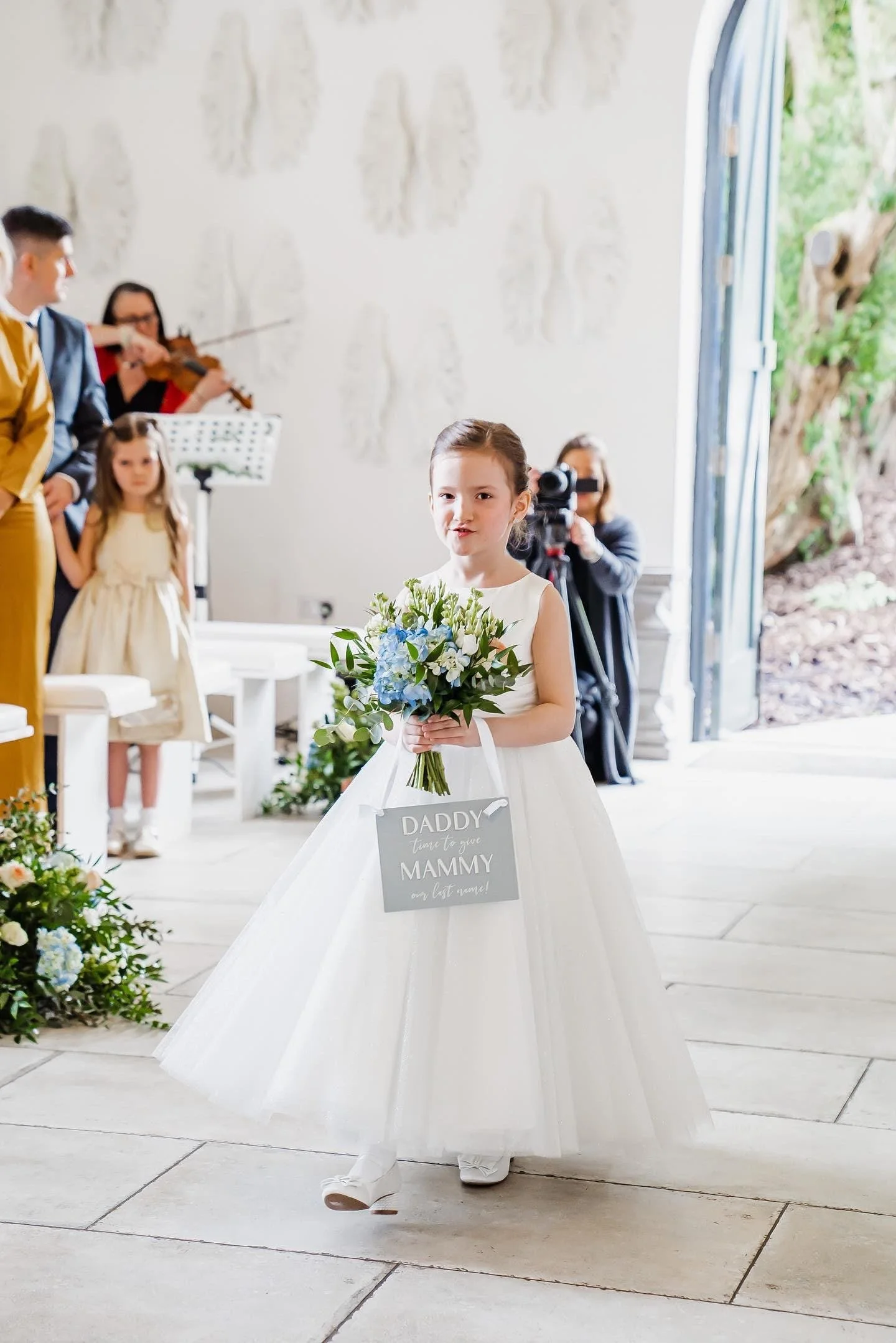 Child walking down a wedding aisle carrying an acrylic hanging ceremony sign