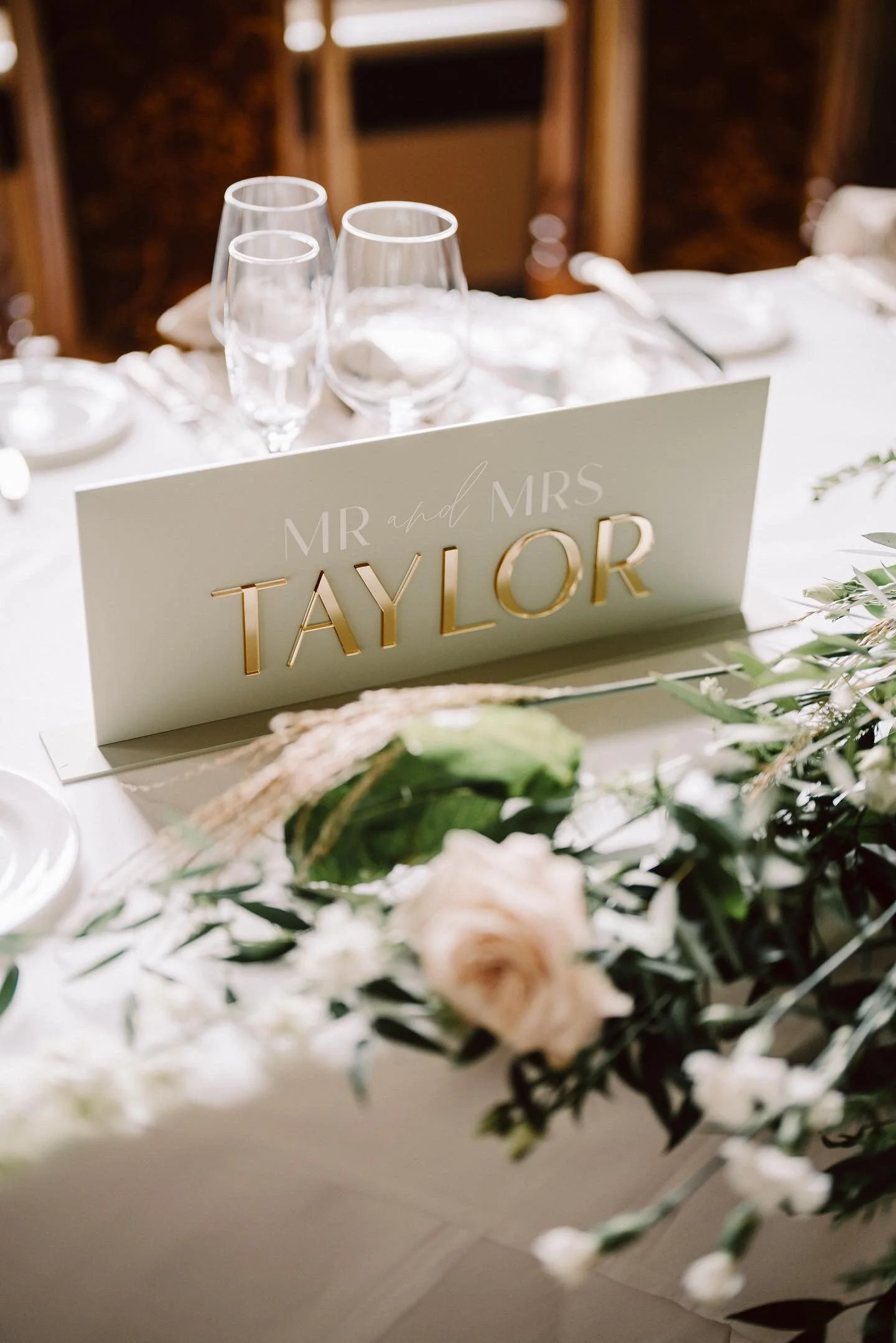 Oyster acrylic wedding top table sign with raised gold mirror Taylor surname on a styled reception table.