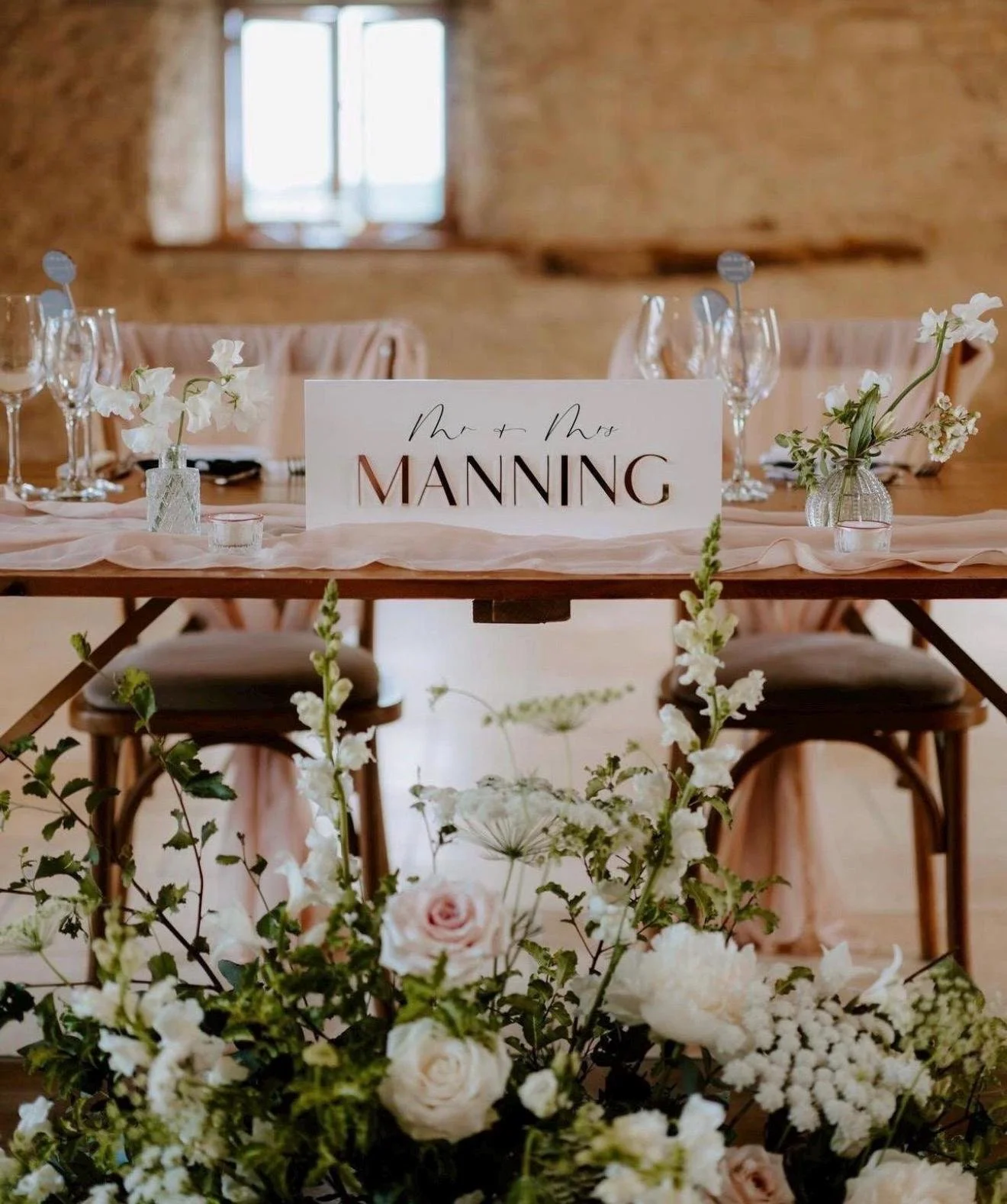 Clear acrylic wedding top table sign with raised gold Manning surname at a rustic reception.