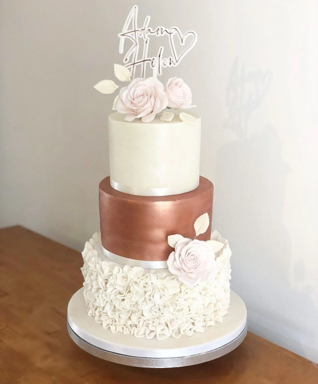 White layered acrylic names and heart topper displayed on a three-tier wedding cake