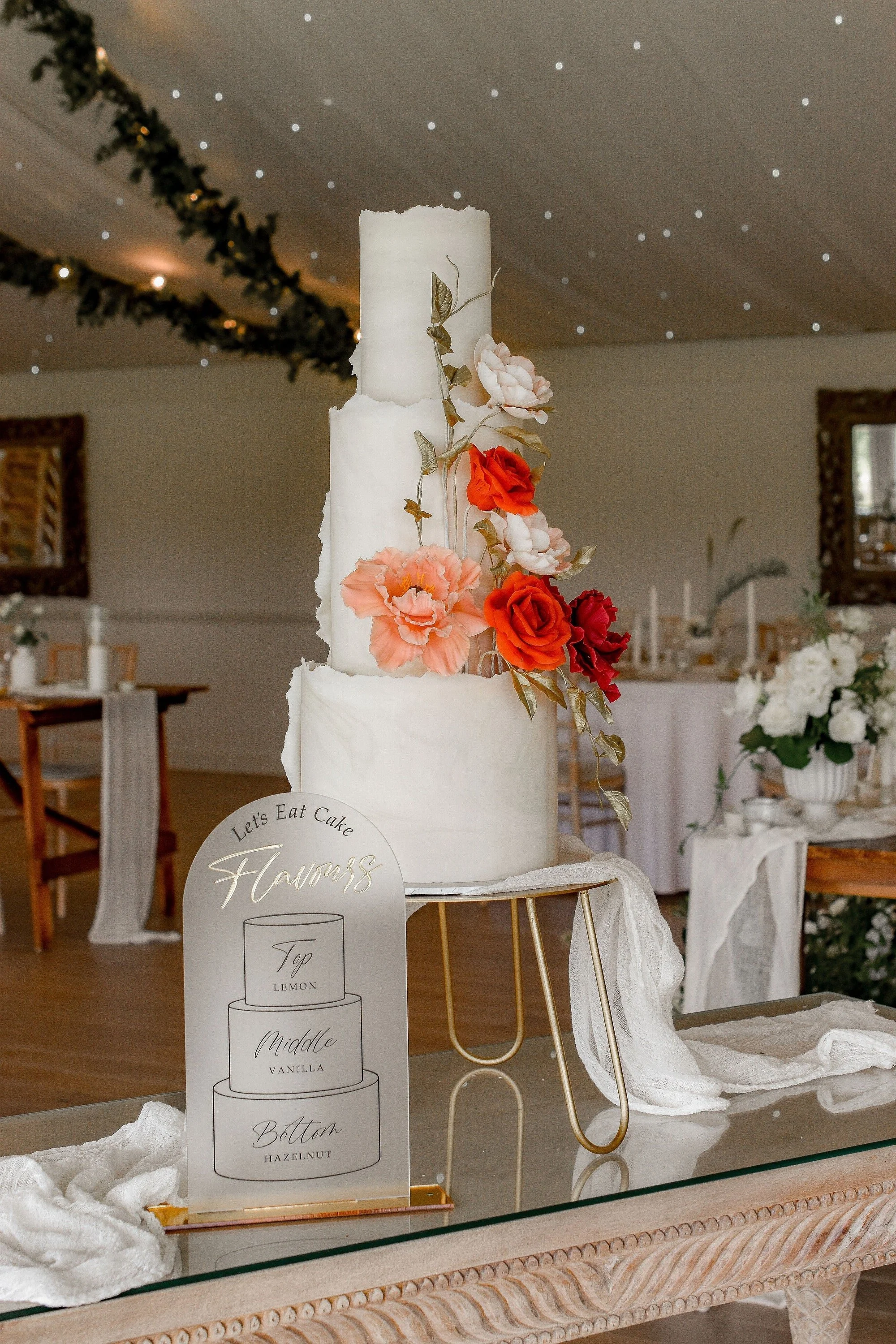 Personalised cake flavour sign displayed beside a tall floral wedding cake at a reception