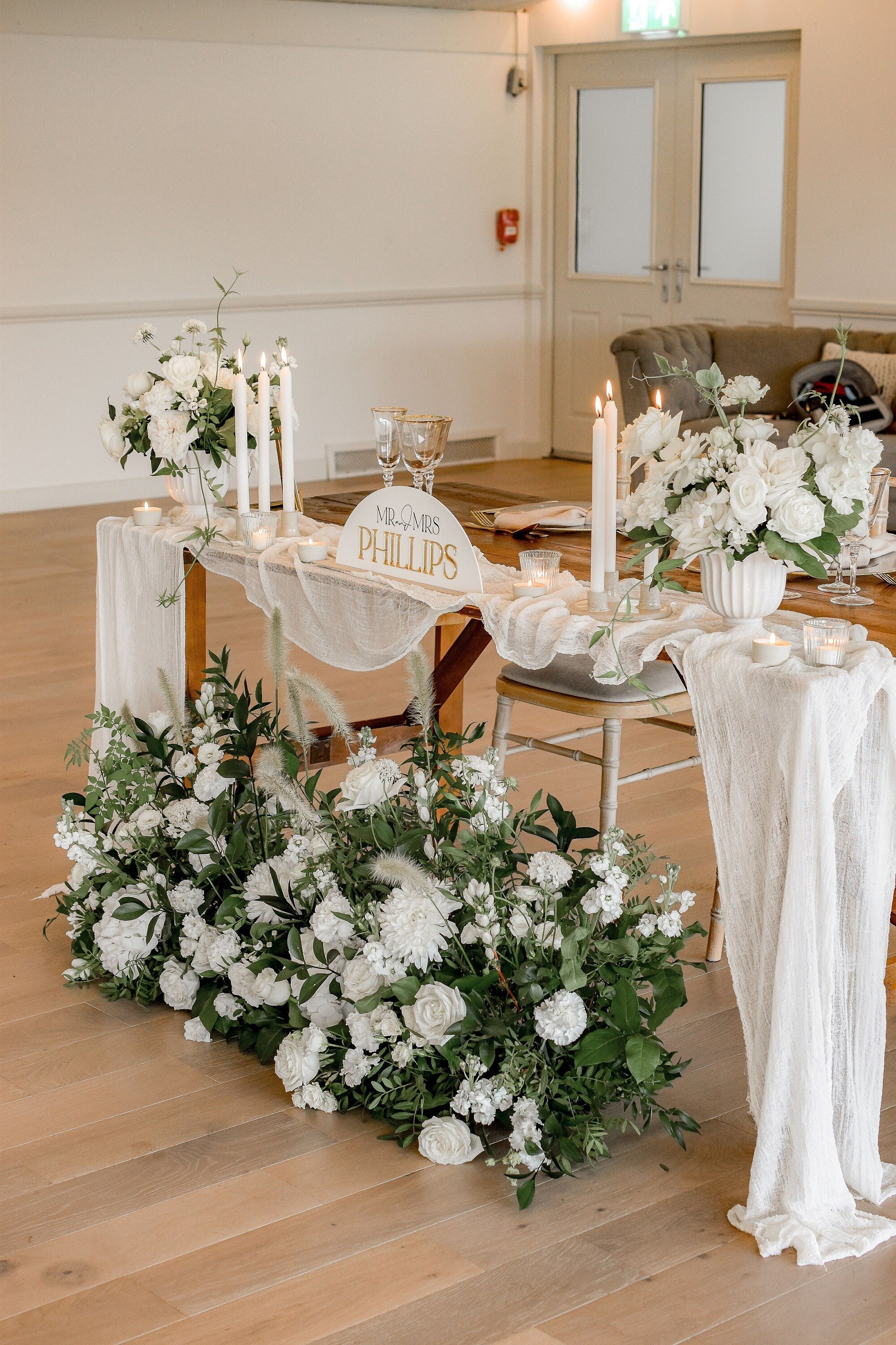 Personalised acrylic surname sign displayed among flowers and candles on a wedding top table