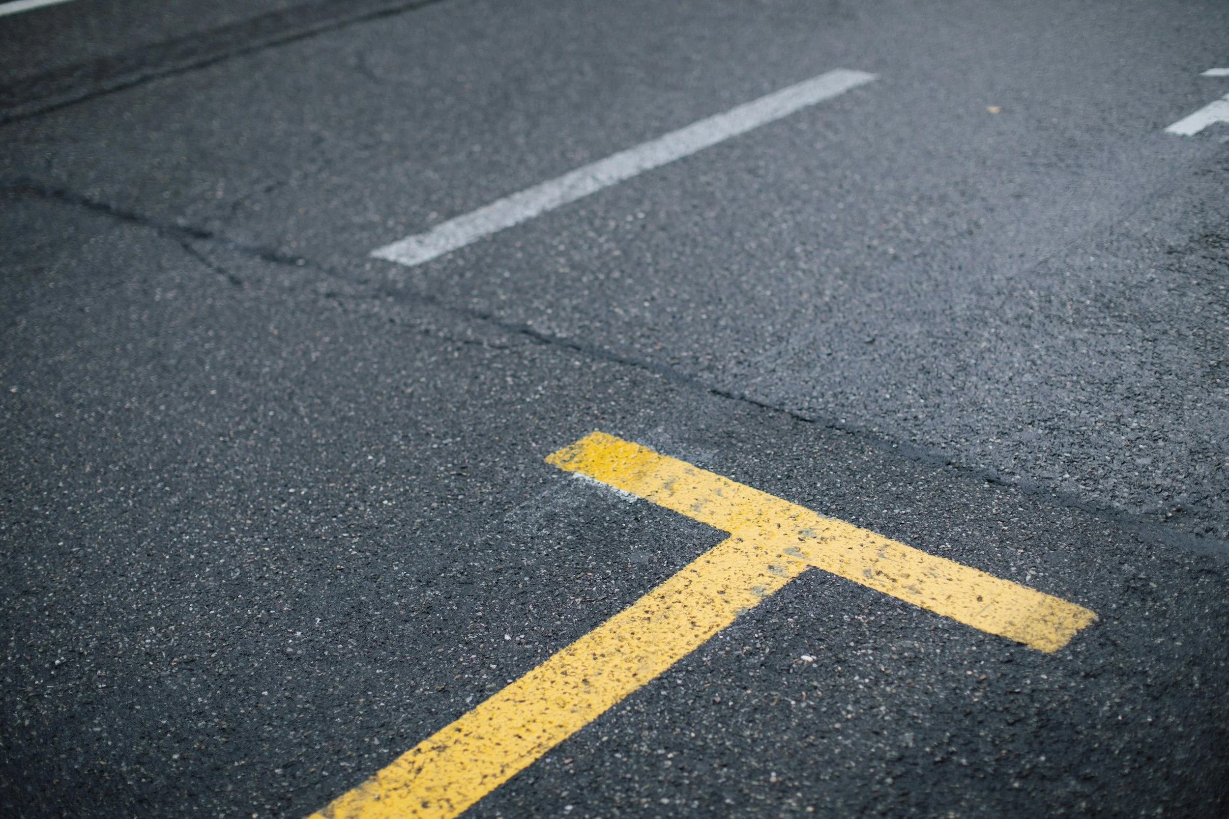 Close-up of a section of asphalt road with white and yellow painted parking space lines.