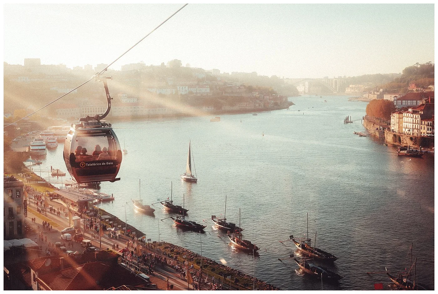 A cable car glides above the Douro River in warm evening light, with boats tracing their way through the water below.