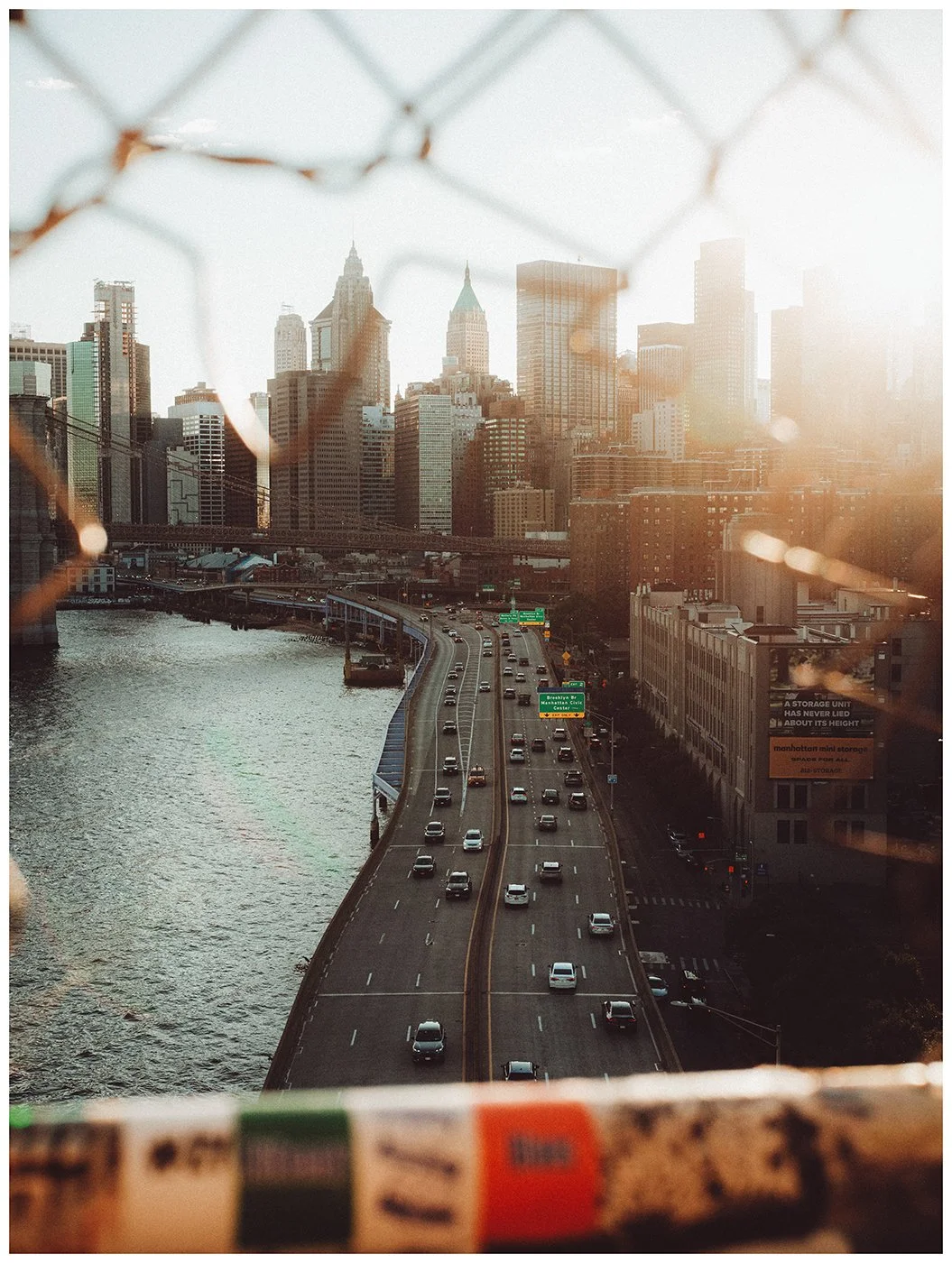 Traffic follows the river toward Lower Manhattan as the skyline fades into warm evening light beyond.
