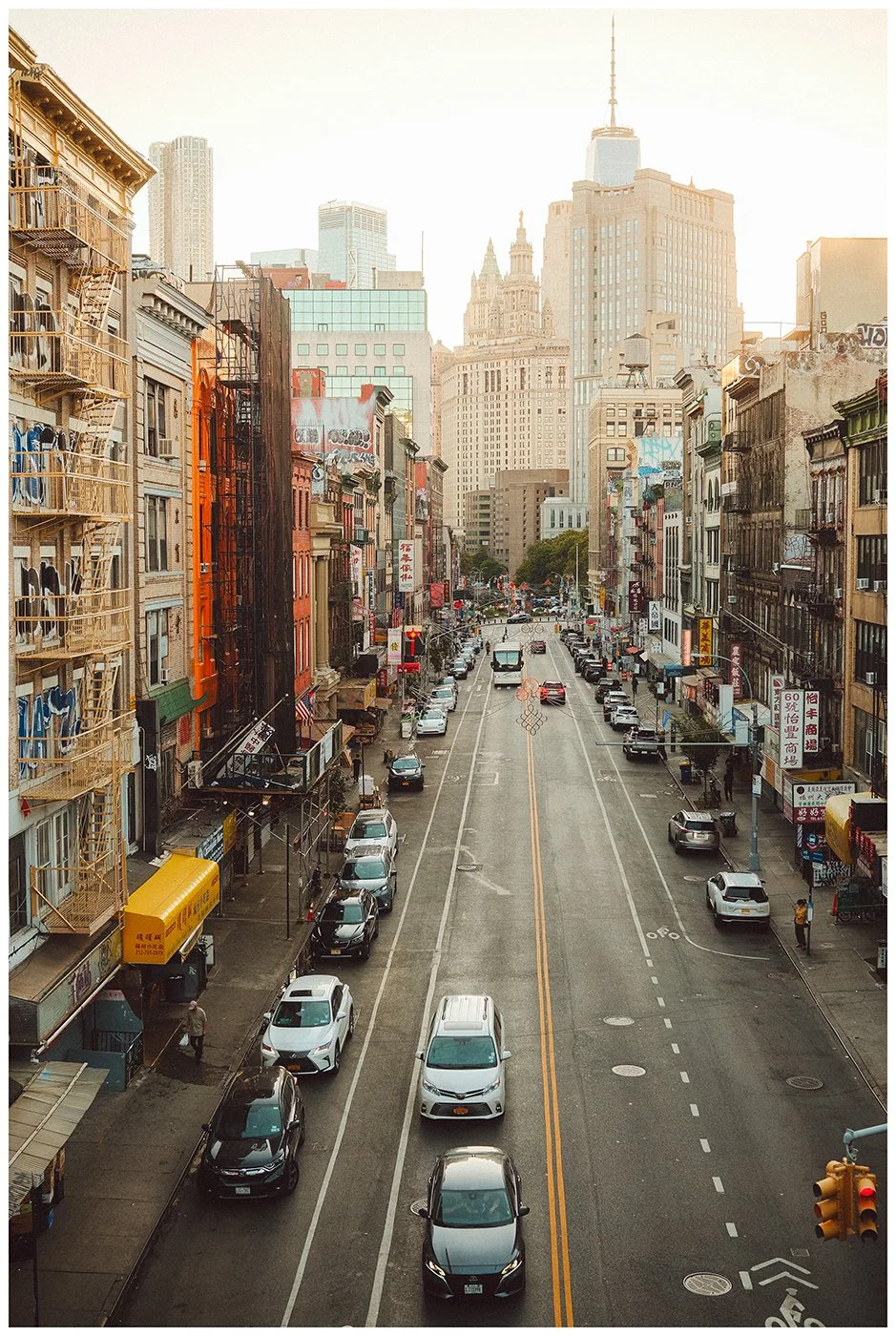 A layered view through Chinatown, where traffic, fire escapes and weathered facades draw the eye toward the towers of Lower Manhattan.