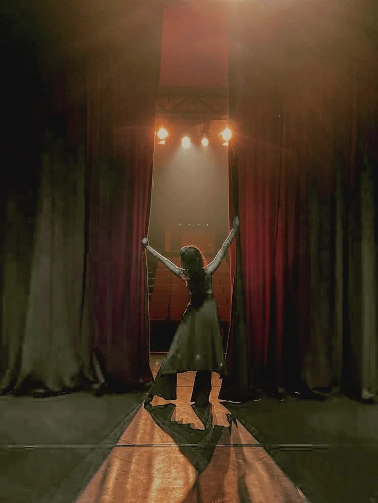 Une femme, qui en dansant, ouvre les rideaux d'une salle de spectacle, découvrant les sièges des spectateurs.