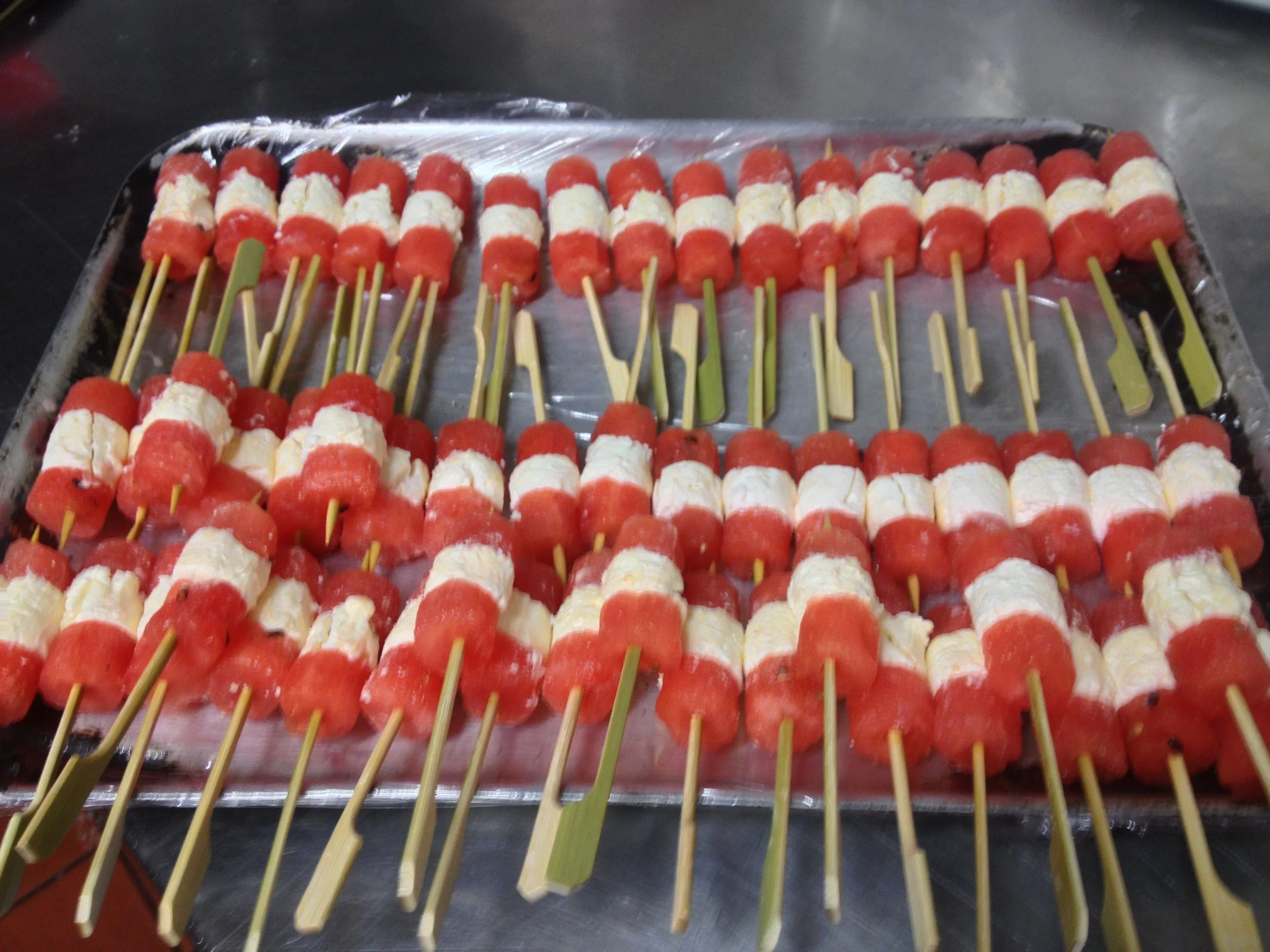 Skewers with watermelon and white cheese pieces arranged on a tray.