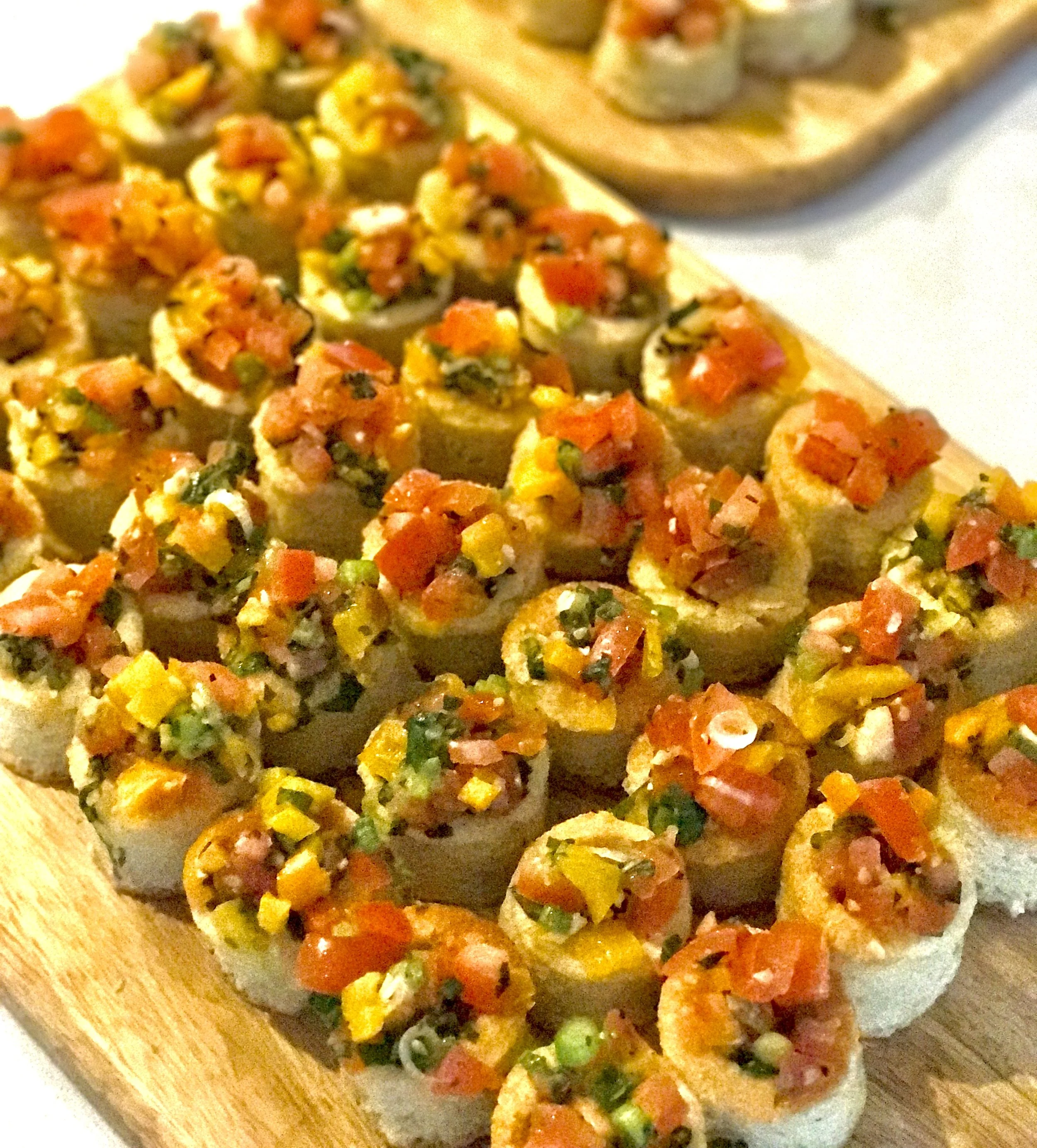 Sushi rolls topped with finely chopped vegetables, including carrots and green onions, served on a wooden board.