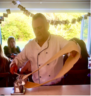 A man lifts a large fish using a towel at a dining restaurant with windows and greenery outside.