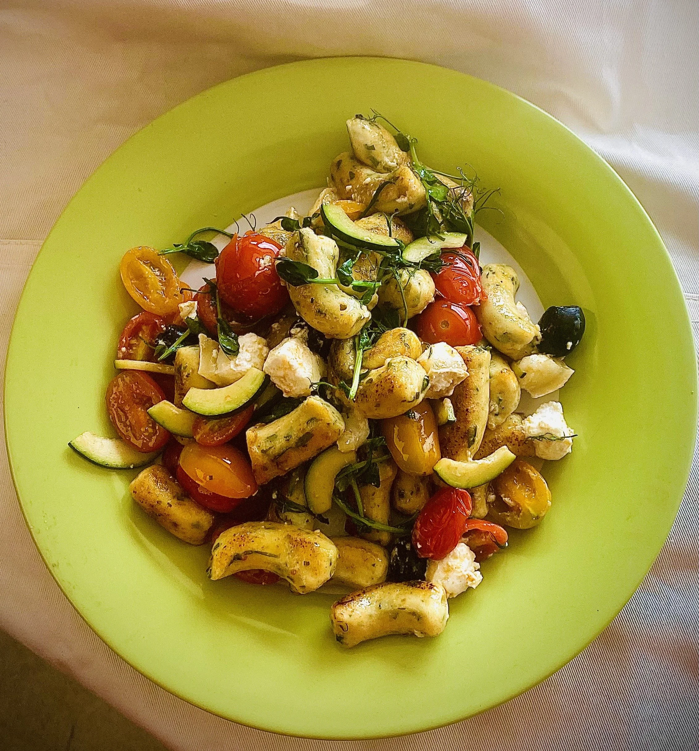 A plate of roasted vegetables including cherry tomatoes, zucchini, and eggplant, garnished with microgreens on a green plate.