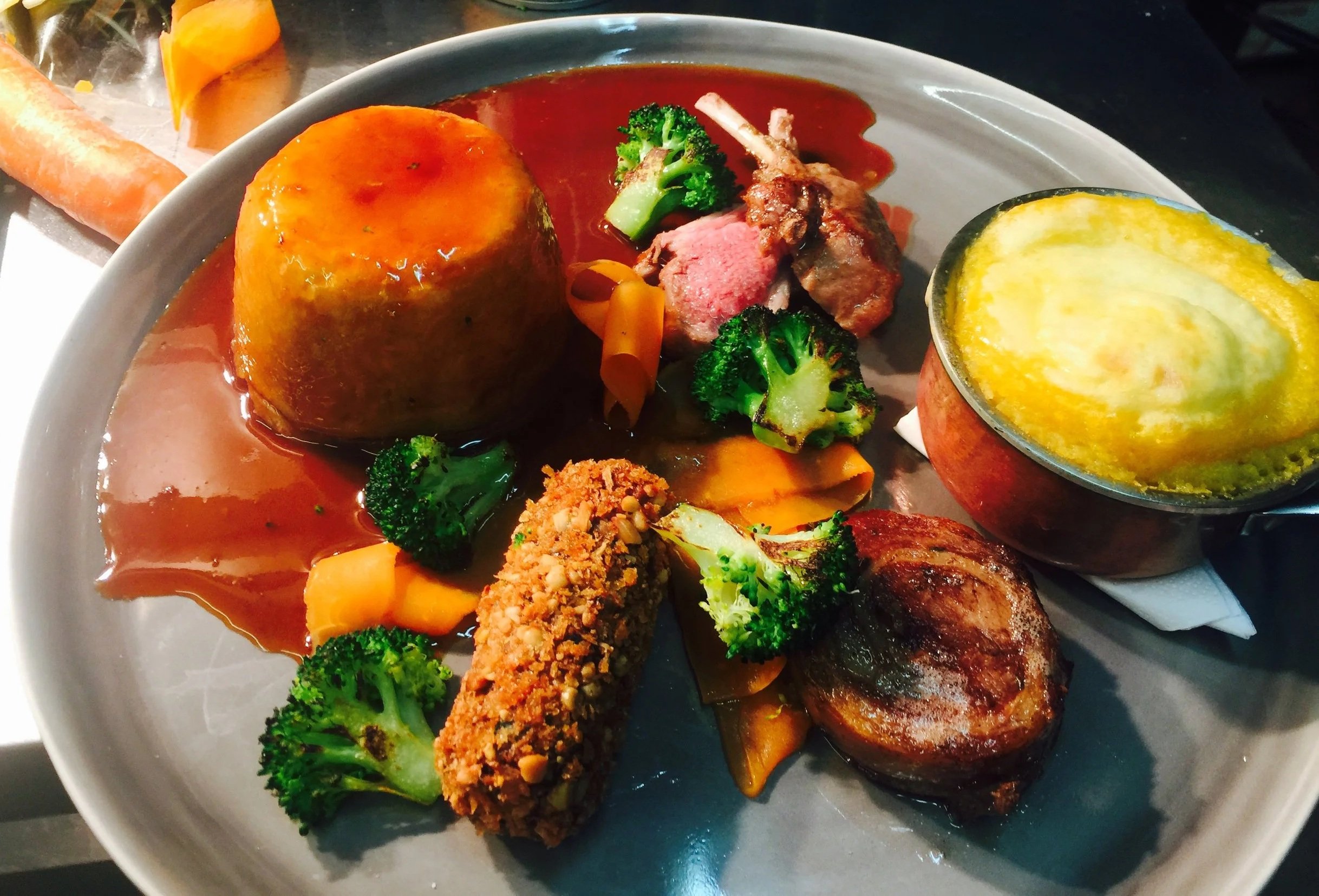 A plate of food with a large baked sweet potato topped with sauce, broccoli, a piece of grilled meat, mashed potatoes in a small dish, and fried vegetables.