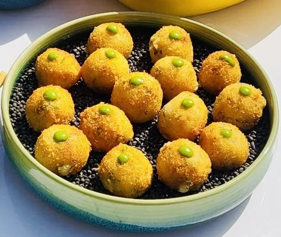Golden-fried balls with green accents on top, arranged in a green bowl filled with small black beads.