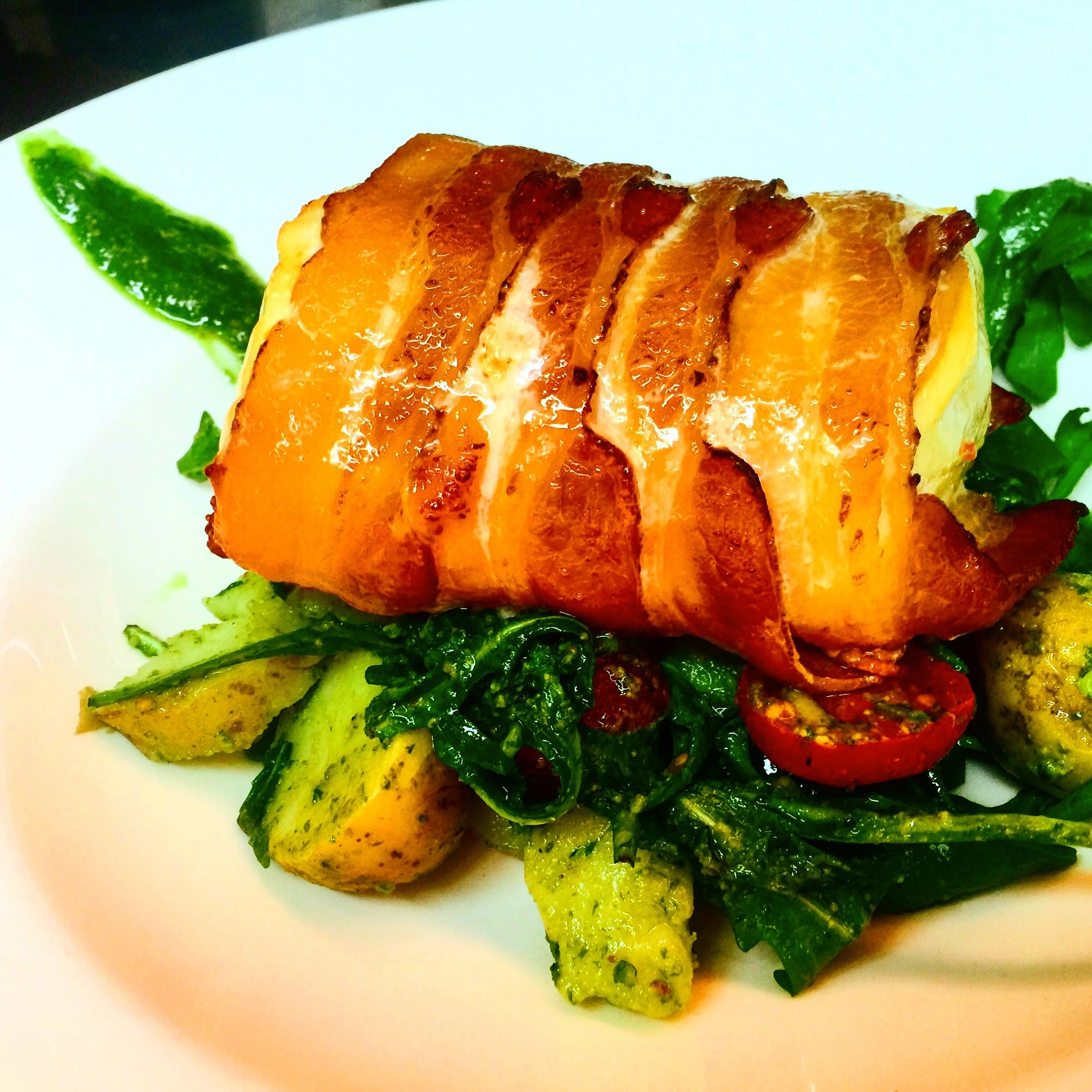Close-up of a plated dish featuring roasted sweet potatoes, green leafy vegetables, and grilled red cherry tomatoes on a white plate.