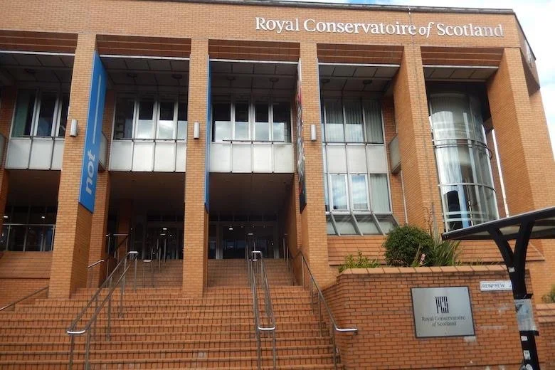 Exterior of the Royal Conservatoire of Scotland building with brick stairs, glass windows, and signs for the institution.