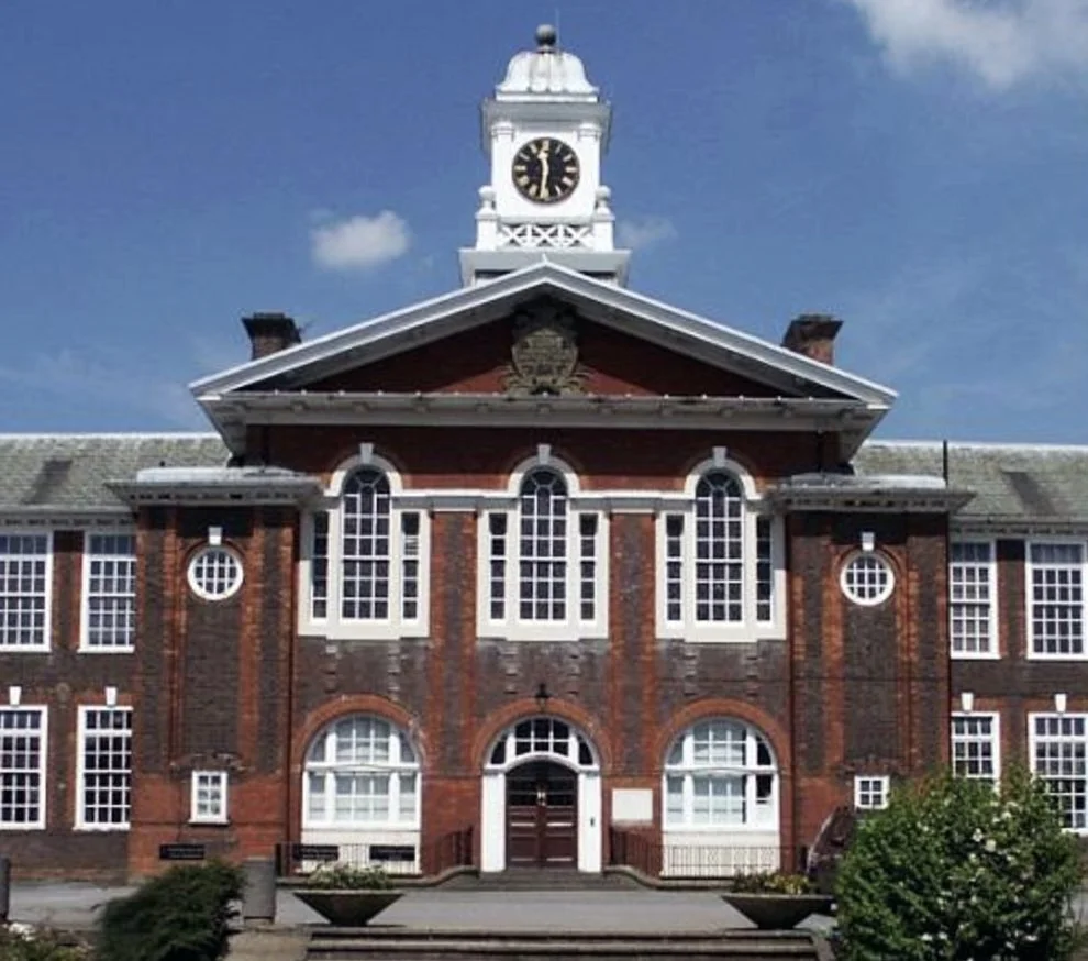 A historic brick building with a clock tower and white trim on a sunny day with a blue sky.