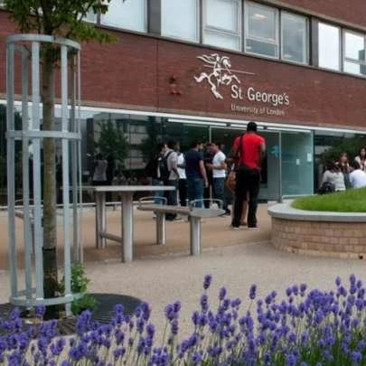 People standing outside St. George's University of London building with purple flowers and trees in the foreground.