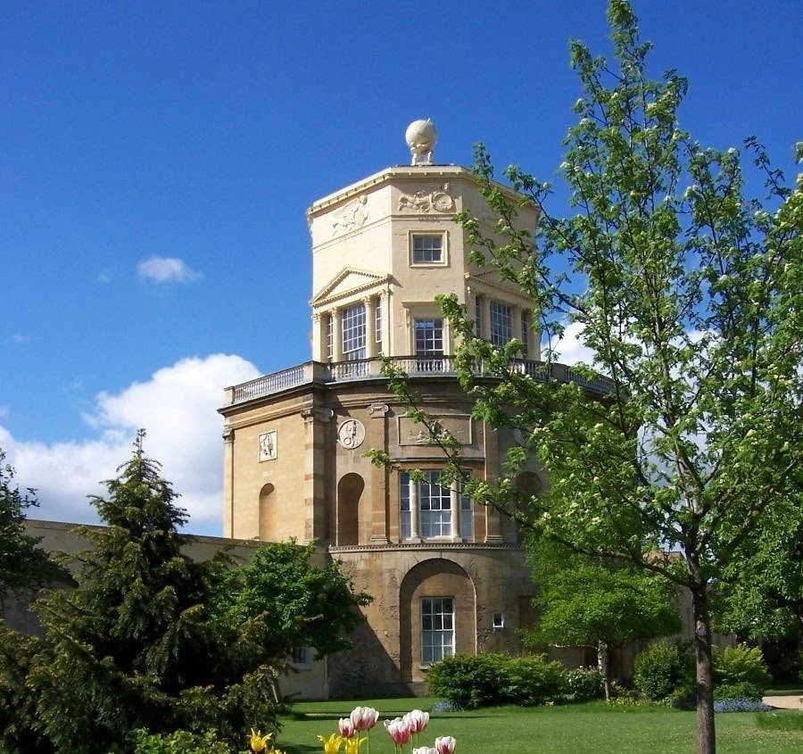 Historic clock tower surrounded by greenery under a blue sky.