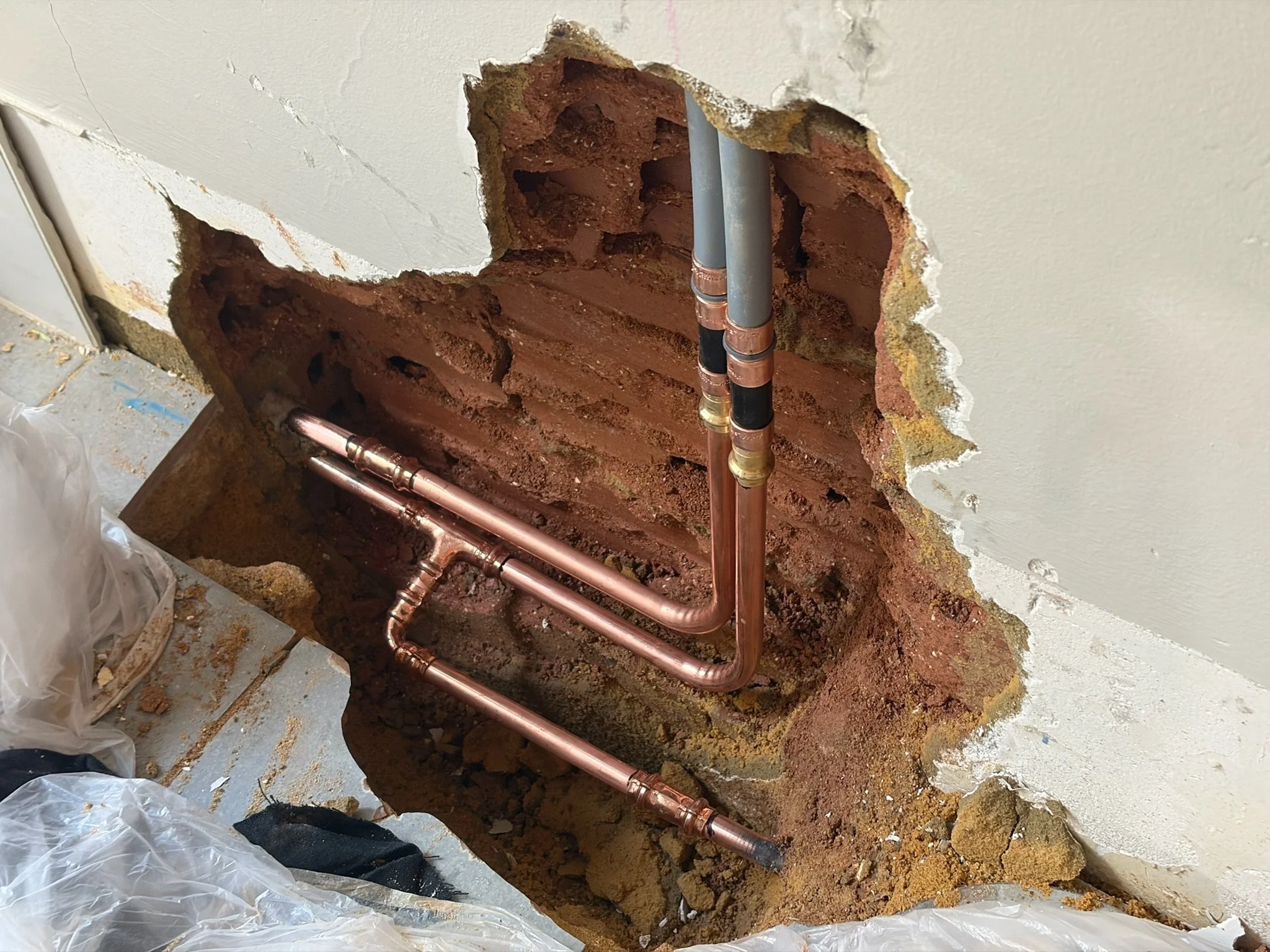 Open wall with exposed pipes and plumbing inside a hole in the wall, surrounded by damaged drywall and insulation.