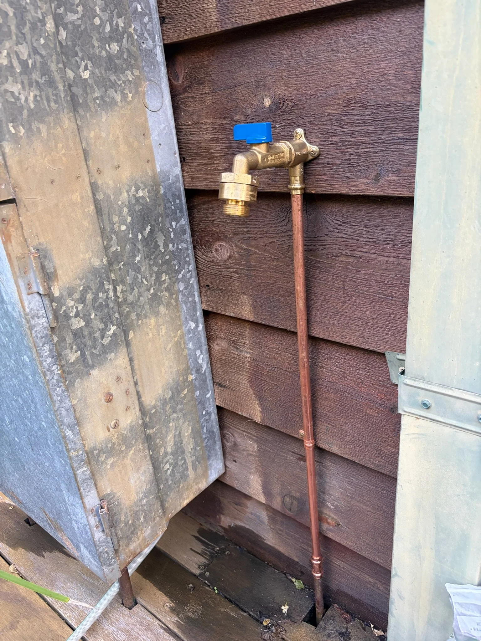 Close-up of a water spigot attached to a brown wooden wall, with a copper pipe connecting to it.